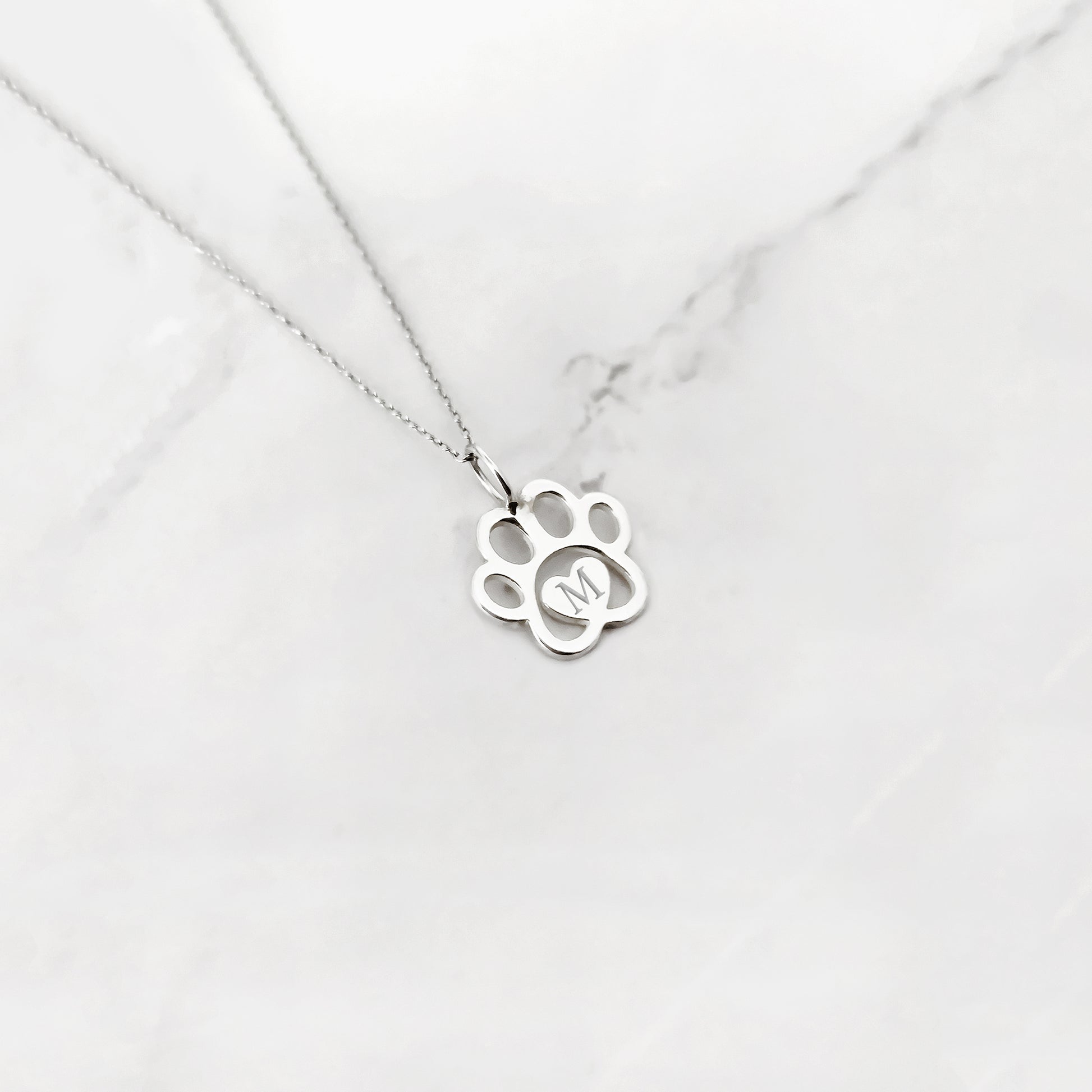 white gold necklace with a dog paw print pendant engraved with a monogram