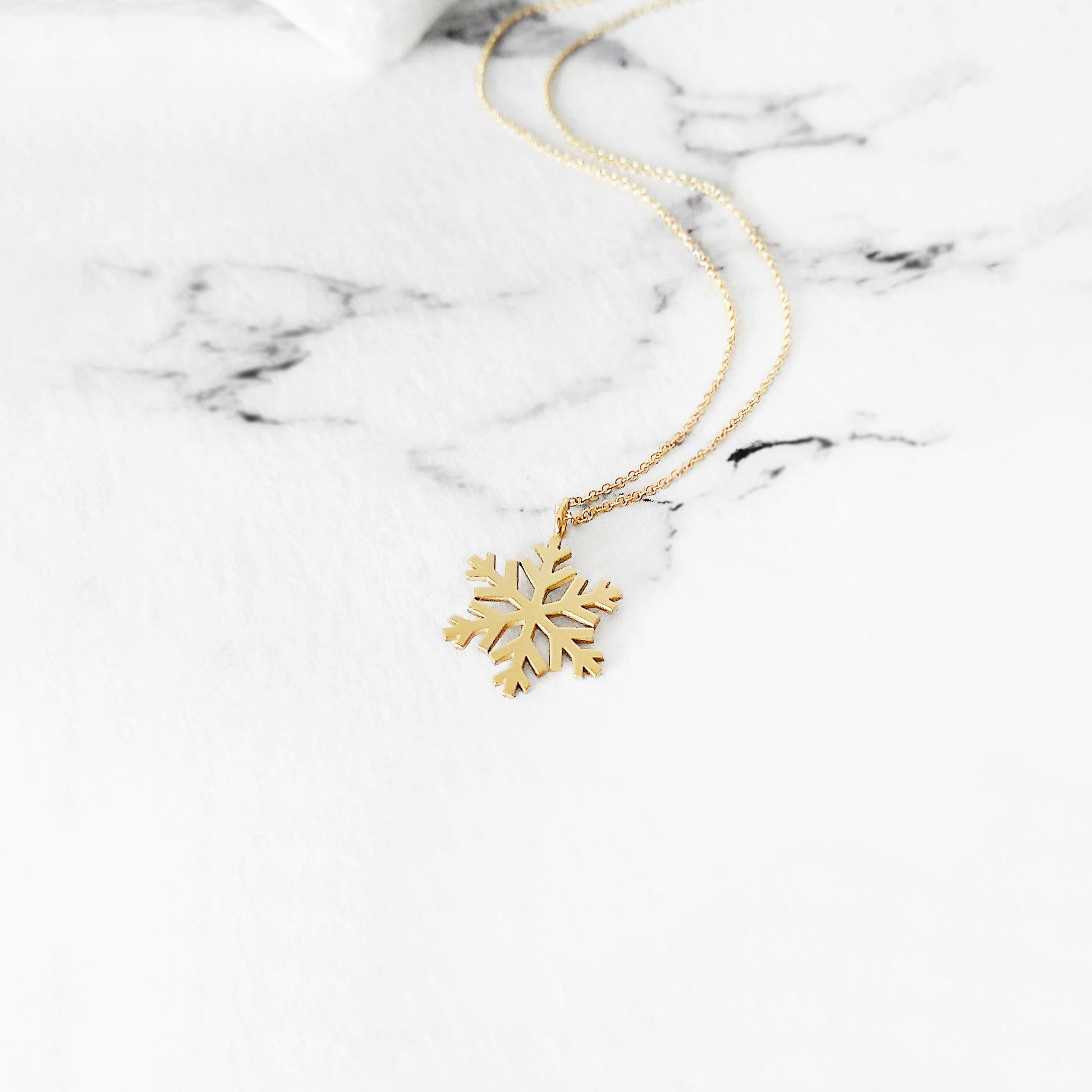 yellow gold necklace with a small pendant in the shape of a snowflake