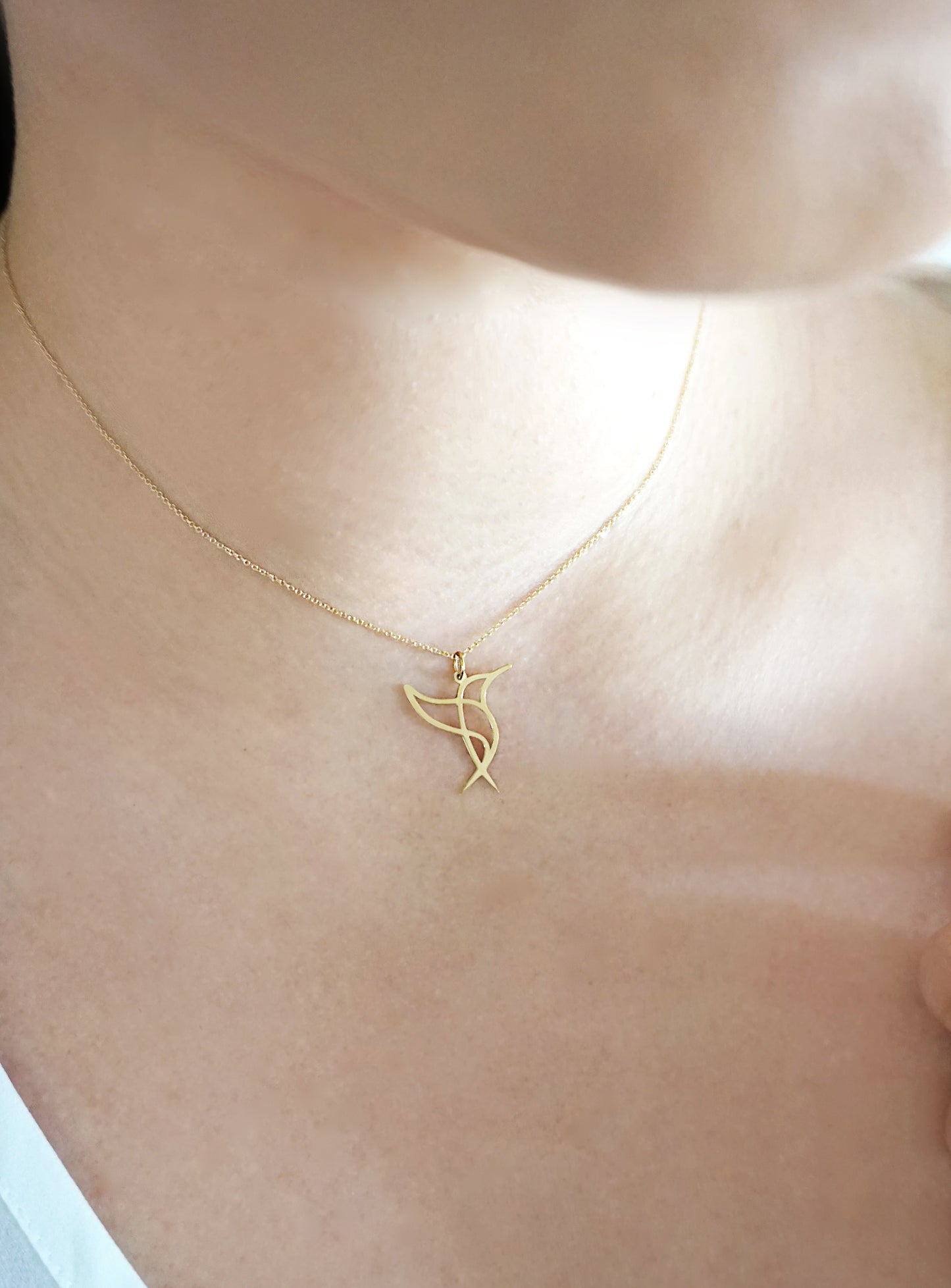 close up of a woman's neck wearing a gold necklace with a cutout pendant in the shape of a hummingbird
