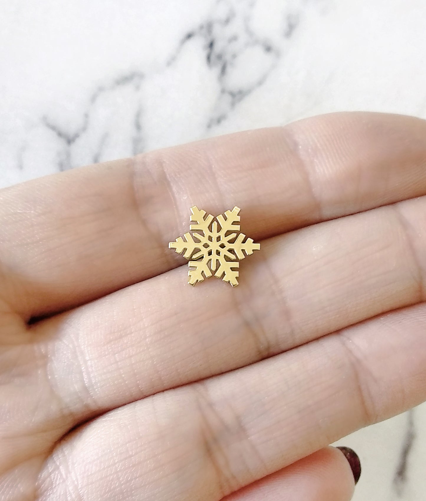 woman's palm holding a gold stud earring in the shape of a snowflake for size reference