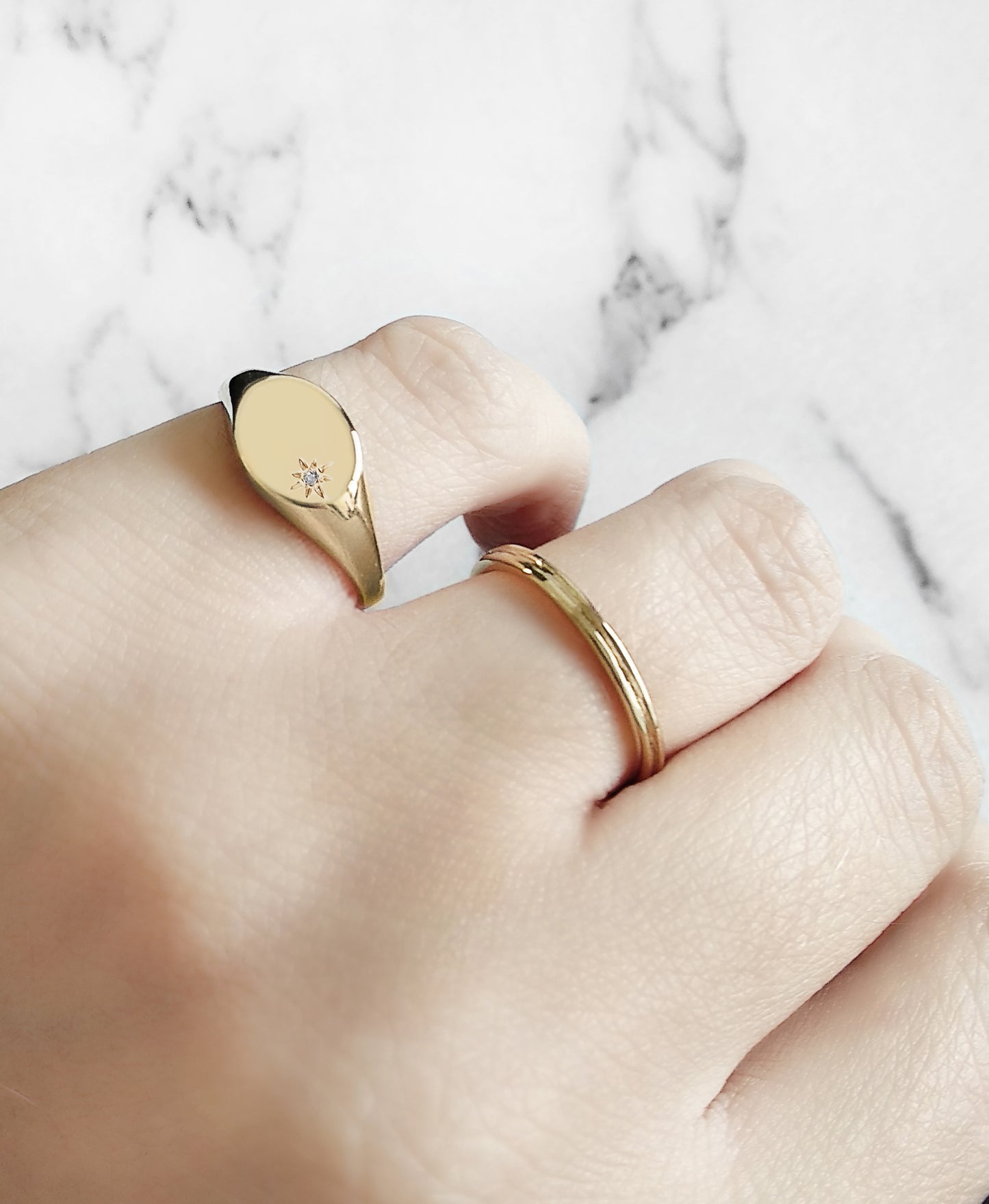 female hand wearing yellow gold oval signet ring set with a tiny diamond with a polaris star setting on her pinky and a simple band in her ring finger