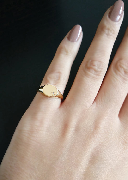 female hand wearing yellow gold oval signet ring set with a tiny diamond with a polaris star setting on her pinky