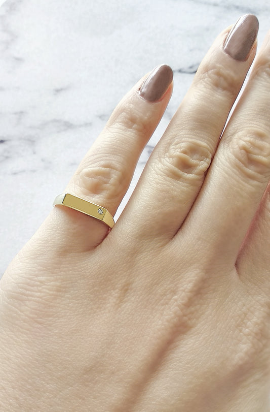 female wearing on her pinky a yellow gold thick bar rectangle signet ring set with a tiny diamond