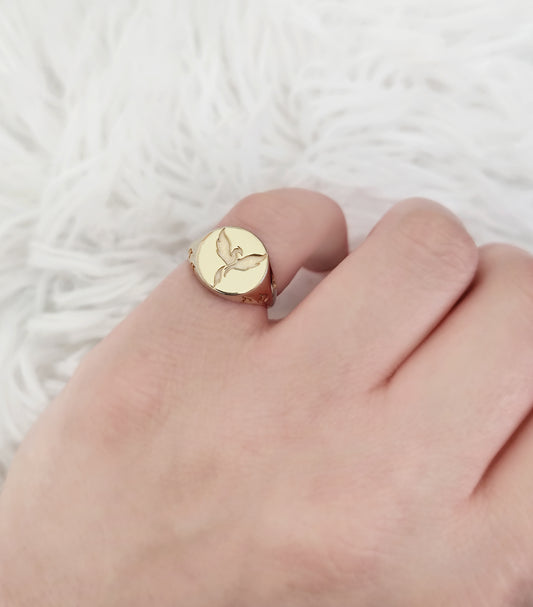 female hand wearing yellow gold polished round signet ring engraved with a phoenix firebird rising with flame cutouts around the base of the ring's head