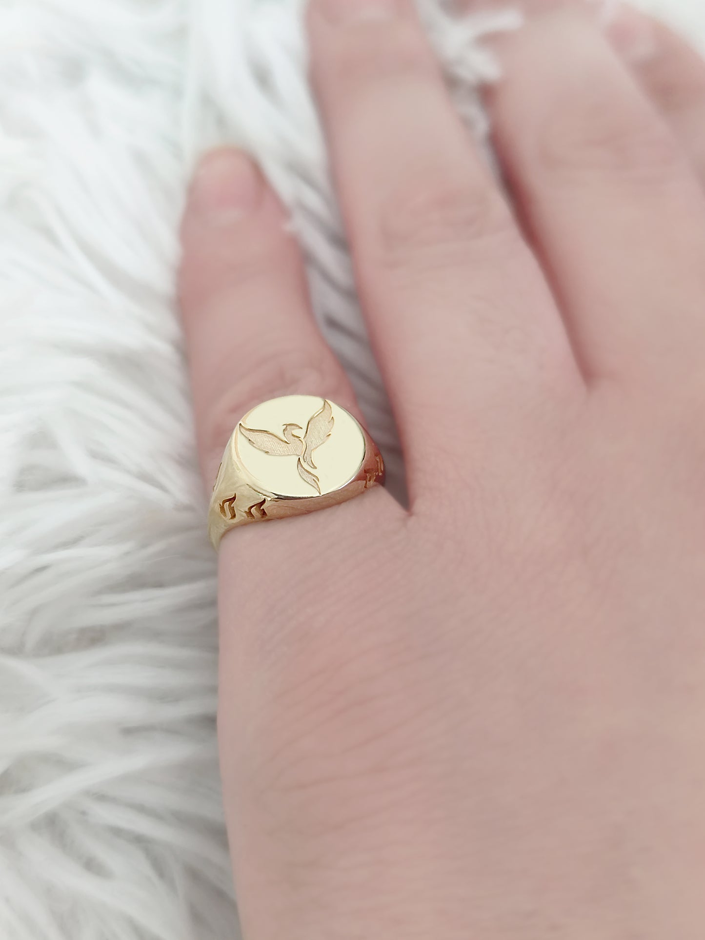 woman's pinky wearing a yellow gold polished round signet ring engraved with a phoenix firebird rising with flame cutouts around the base of the ring's head