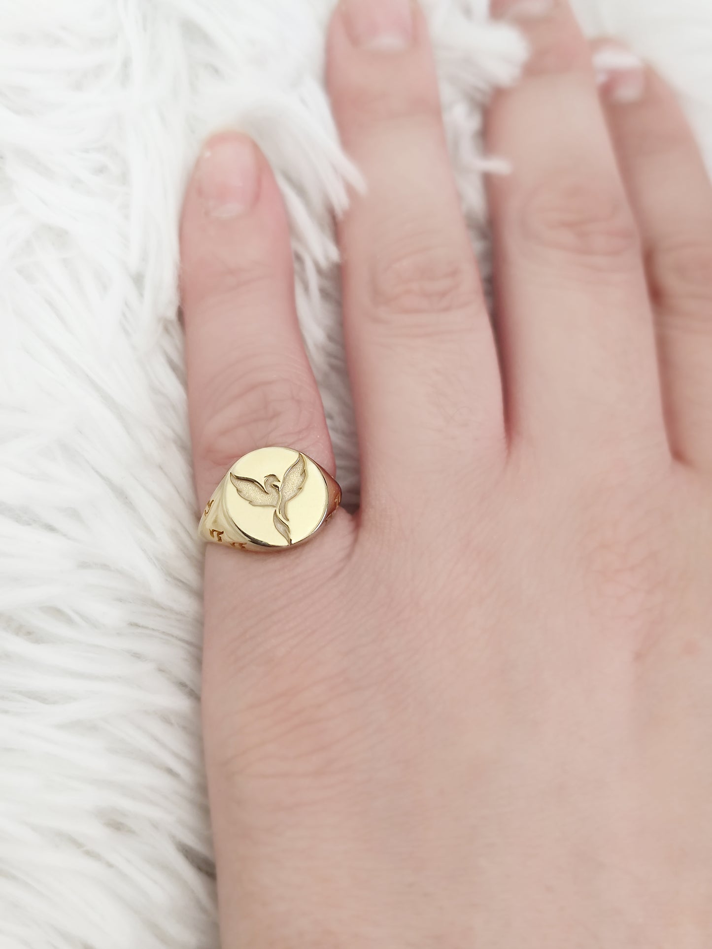 female hand wearing on her pinky a yellow gold polished round signet ring engraved with a phoenix firebird rising with flame cutouts around the base of the ring's head