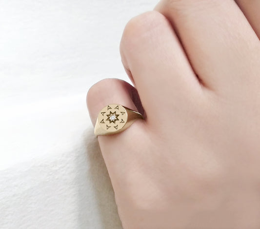 woman wearing on her pinky a solid yellow gold round signet ring with a north star starburst design and a diamond on the center