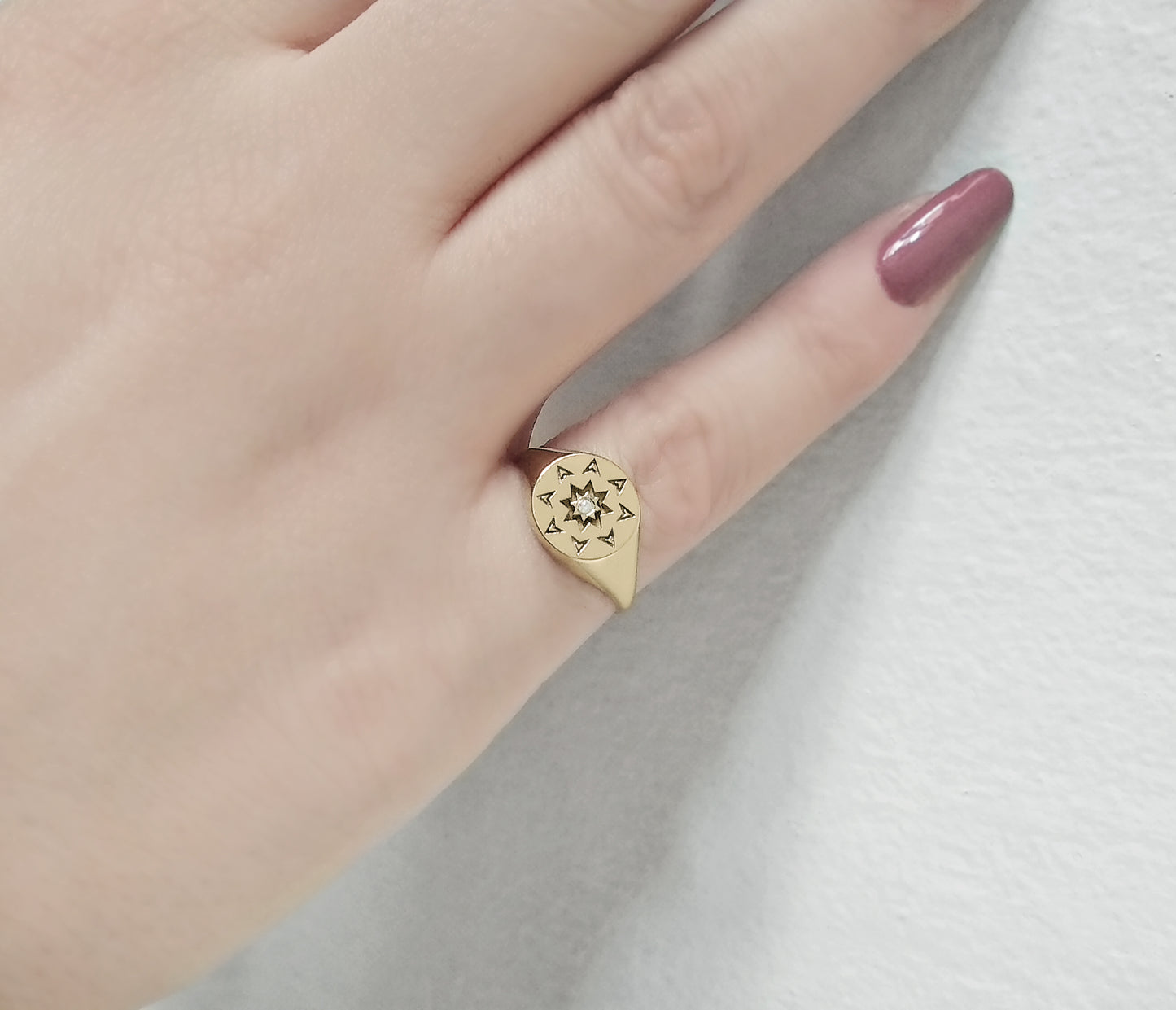 woman's hand wearing a solid yellow gold round signet ring with a north star starburst design and a diamond on the center