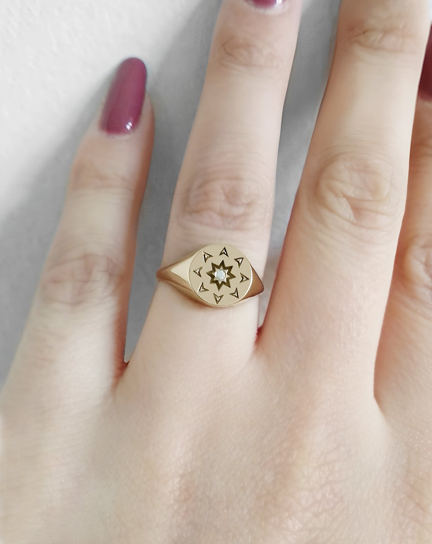 female wearing on her ring finger a solid yellow gold round signet ring with a north star starburst design and a diamond on the center