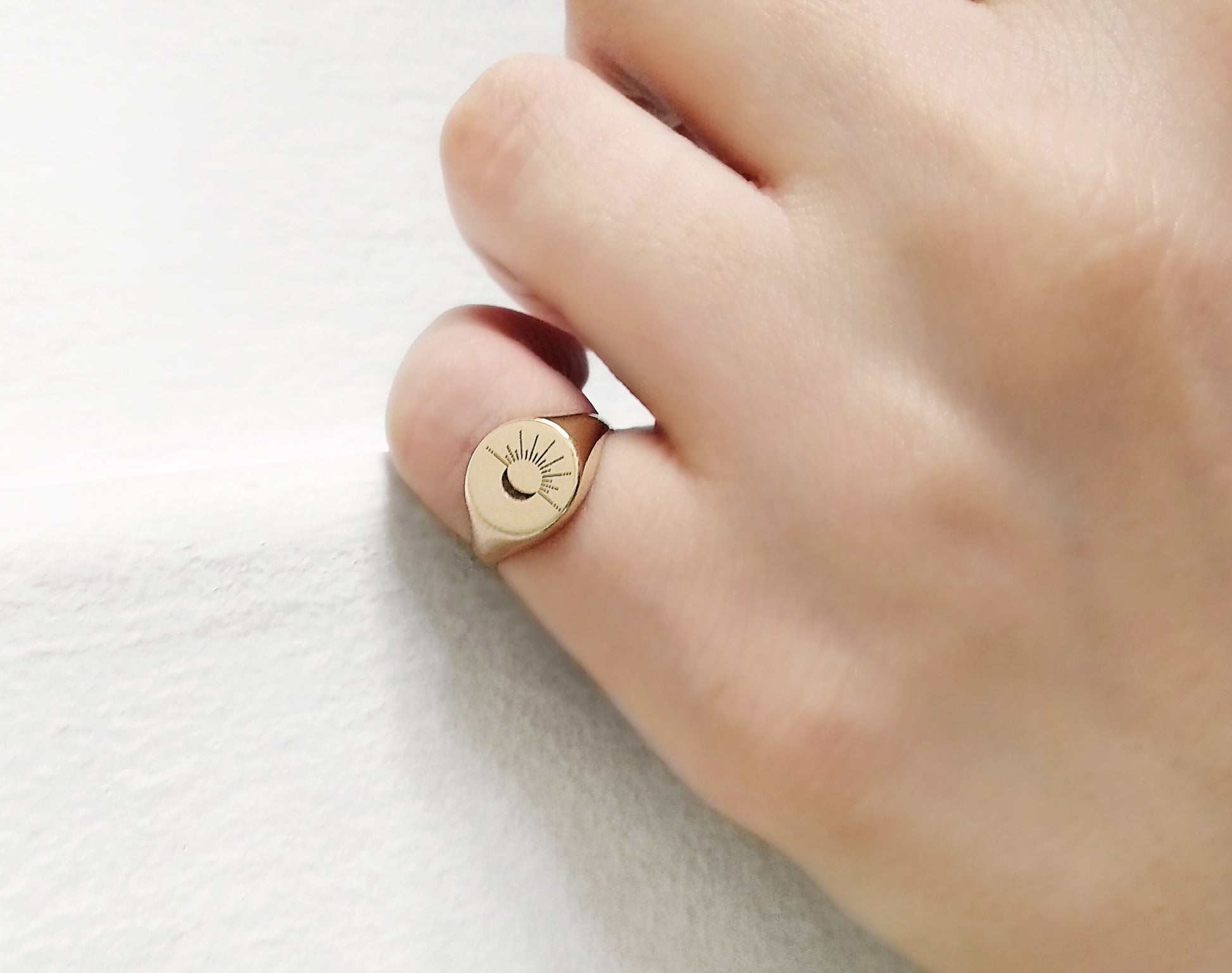 female hand wearing solid yellow gold round signet ring engraved with the sun and moon on her pinky