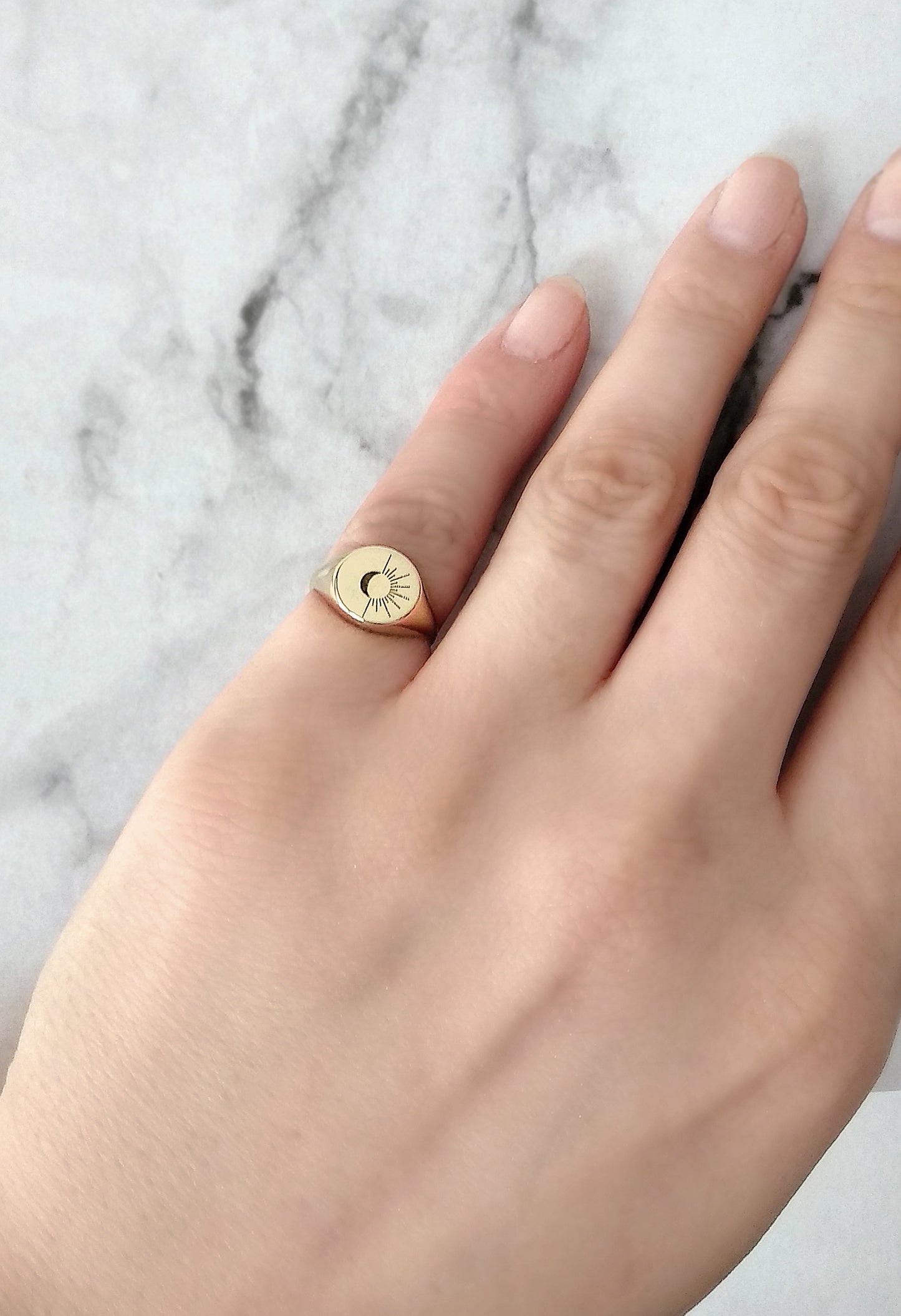female hand wearing solid yellow gold round signet ring engraved with the sun and moon on her pinky