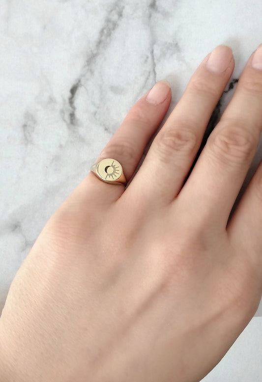 female hand wearing solid yellow gold round signet ring engraved with the sun and moon on her pinky