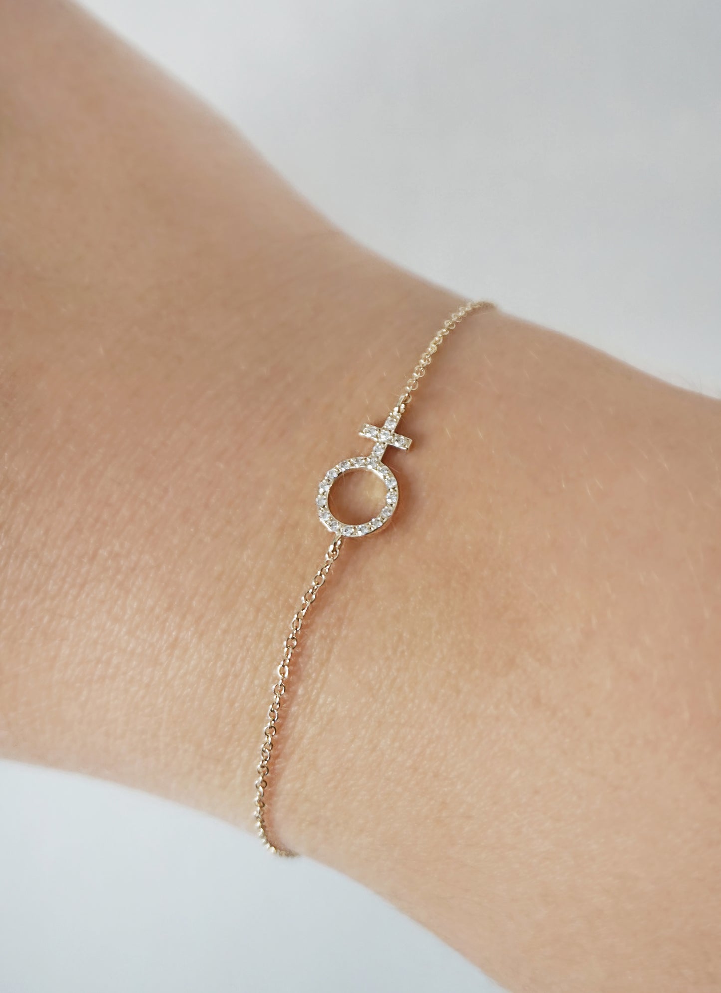 woman's wrist wearing a yellow gold bracelet with a venus female symbol charm set with tiny diamonds