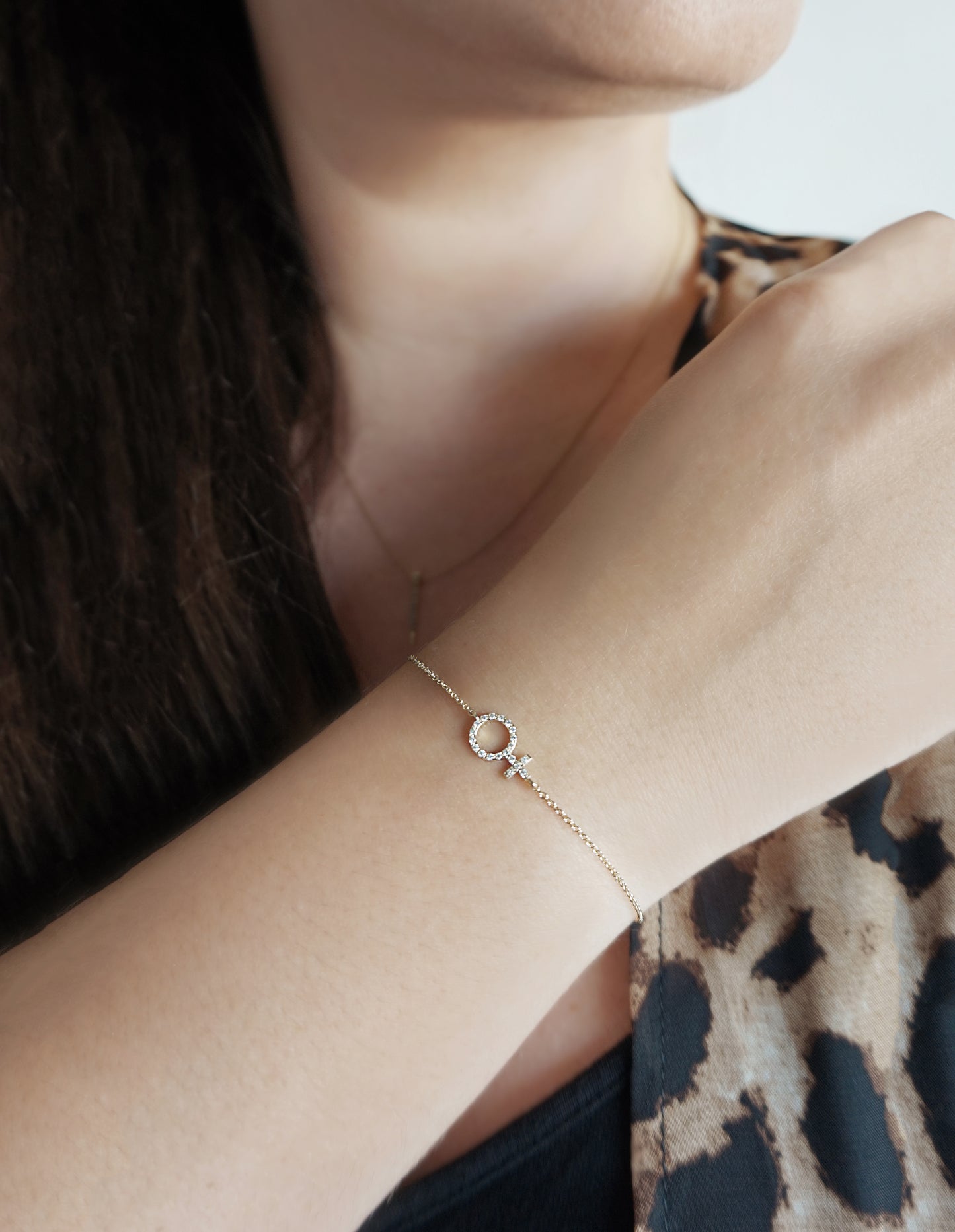 female wearing a solid yellow gold bracelet with a venus female symbol charm set with tiny diamonds