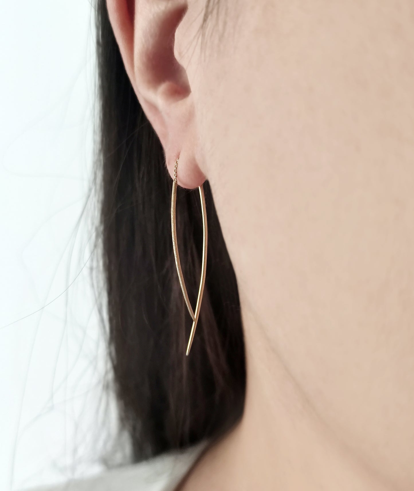 close up of a woman's ear wearing a gold swing threader earring with one matte curved bar and one longer polished curved bar