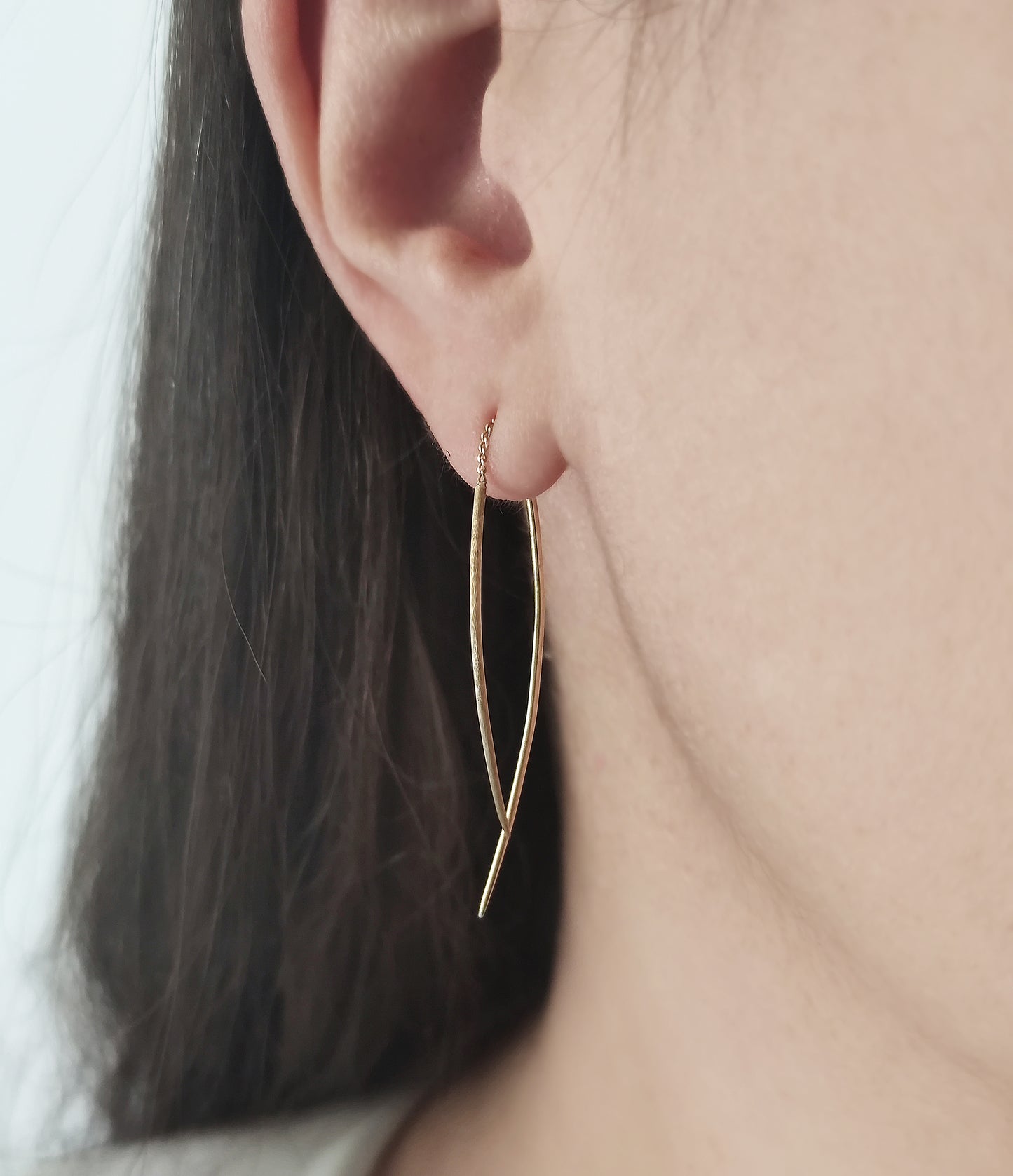 female wearing yellow gold swing threader earring with one matte curved bar and one longer polished curved bar