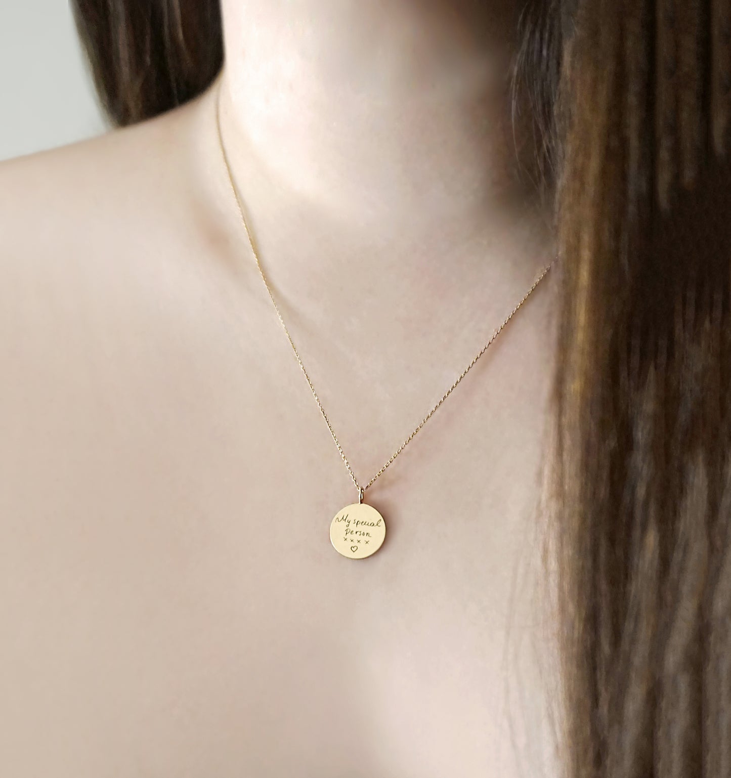 gold necklace with a round pendant with custom handwritten engraving on a female model