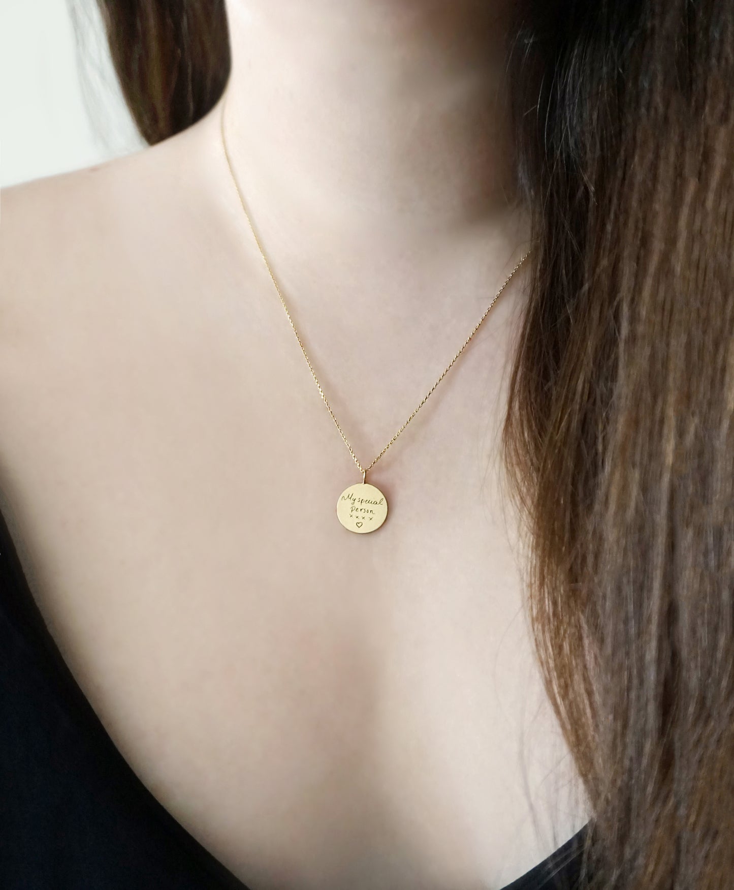 gold necklace with a round pendant with custom handwritten engraving on a female's neck