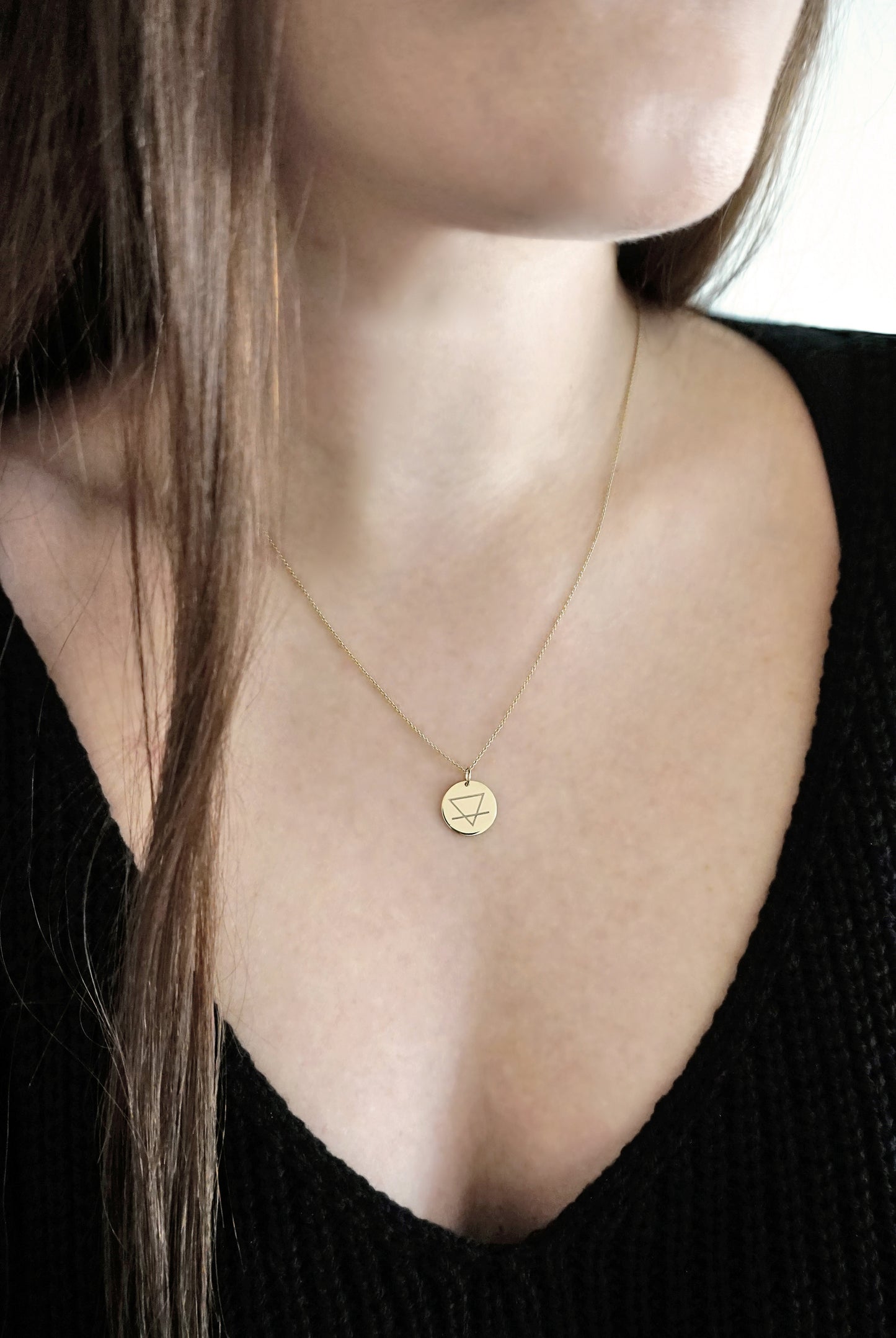 female wearing a yellow gold necklace with a 14mm disc pendant engraved with the earth element