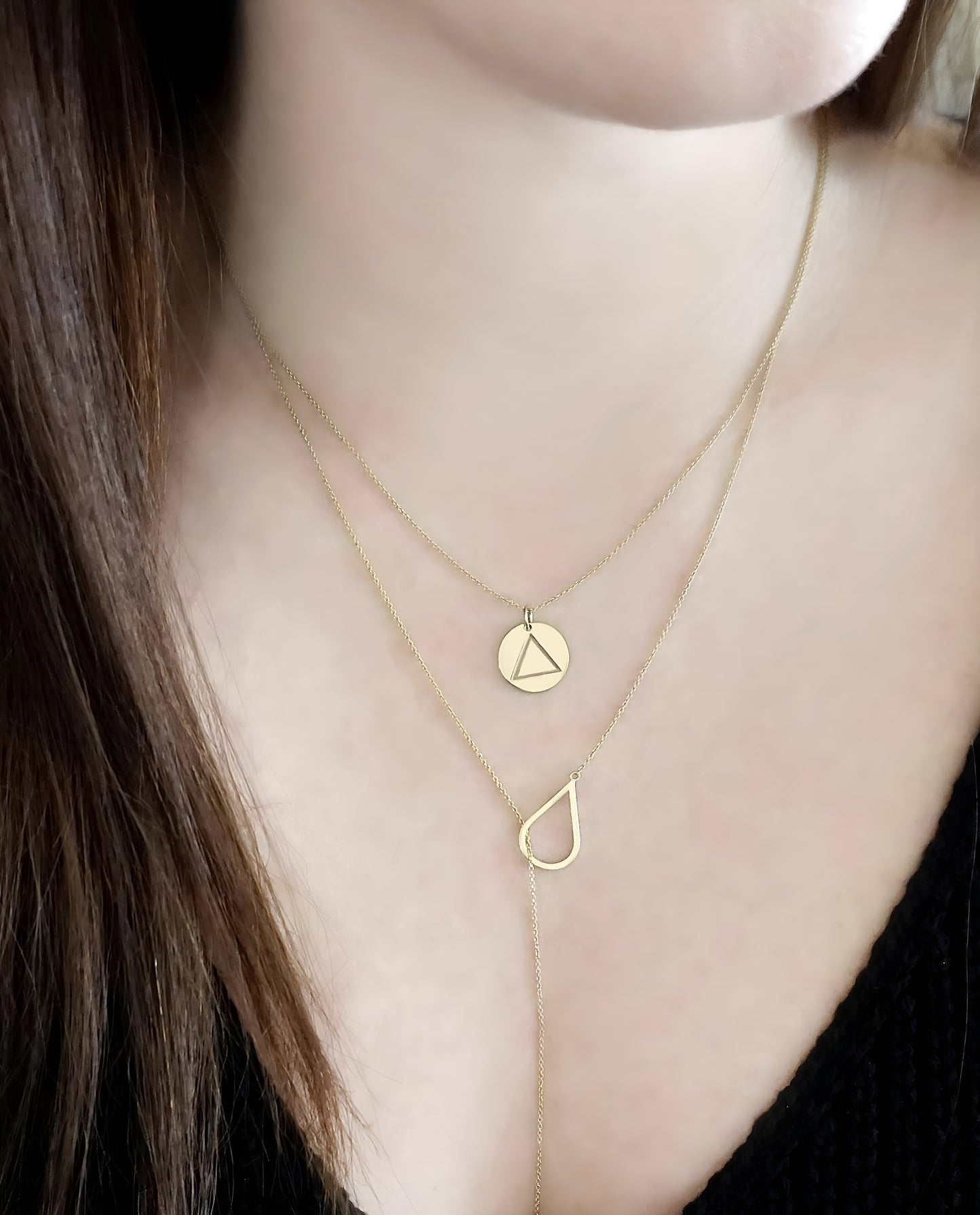 close up of a woman's neck wearing a yellow gold necklace with a 14mm disc pendant engraved with the fire element symbol layered with a lariat necklace