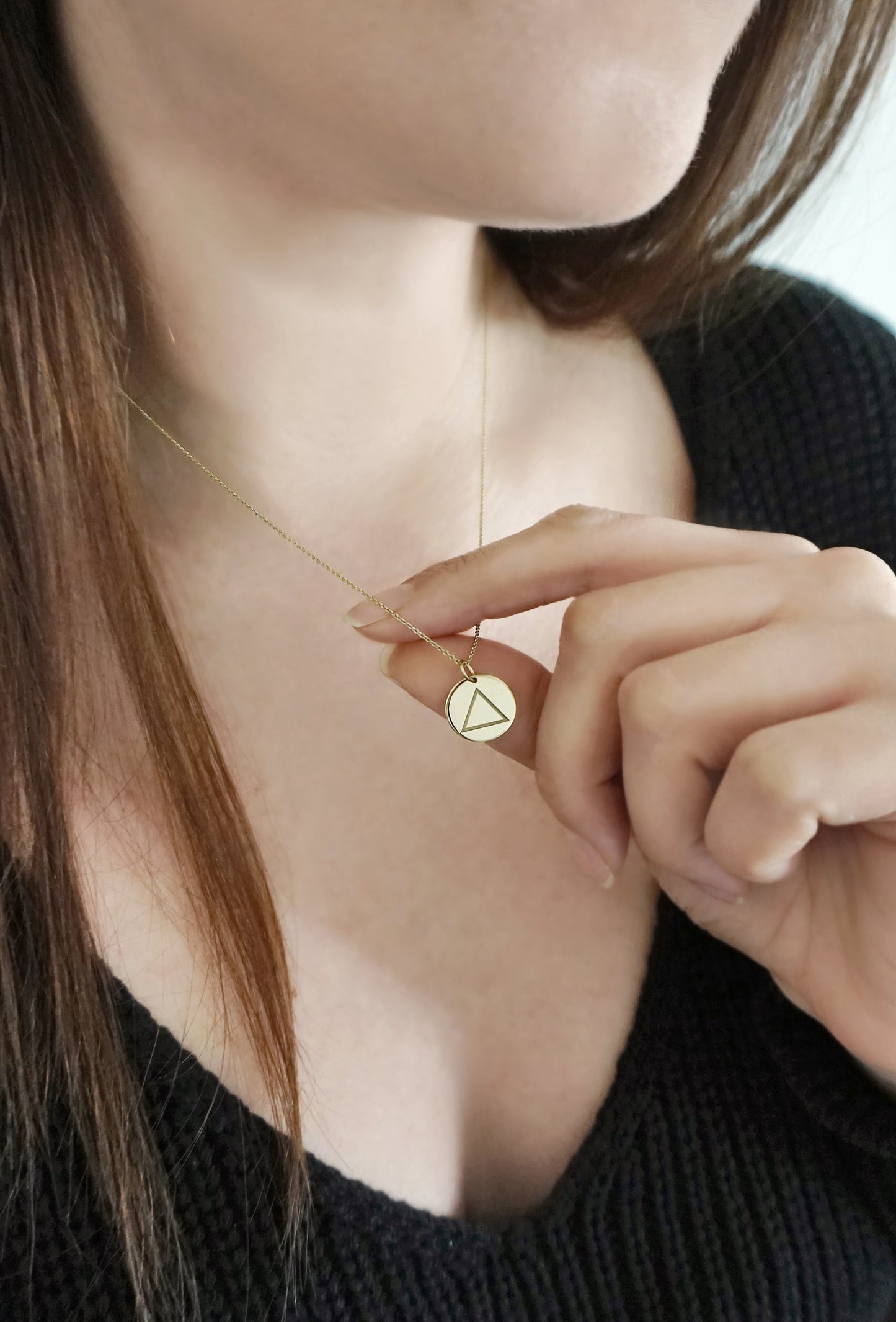 female wearing and holding a yellow gold necklace with a 14mm disc pendant engraved with the fire element symbol