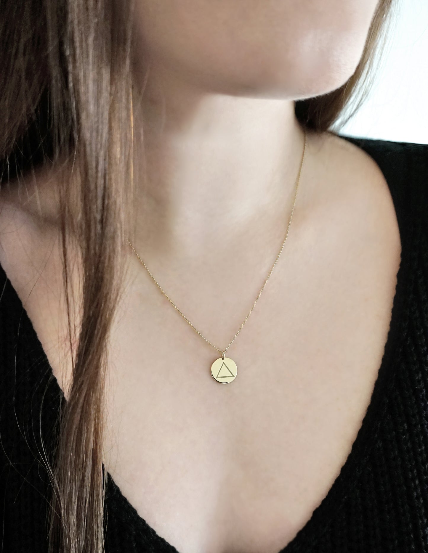 close up of a woman's neck wearing a yellow gold necklace with a 14mm disc pendant engraved with the fire element symbol