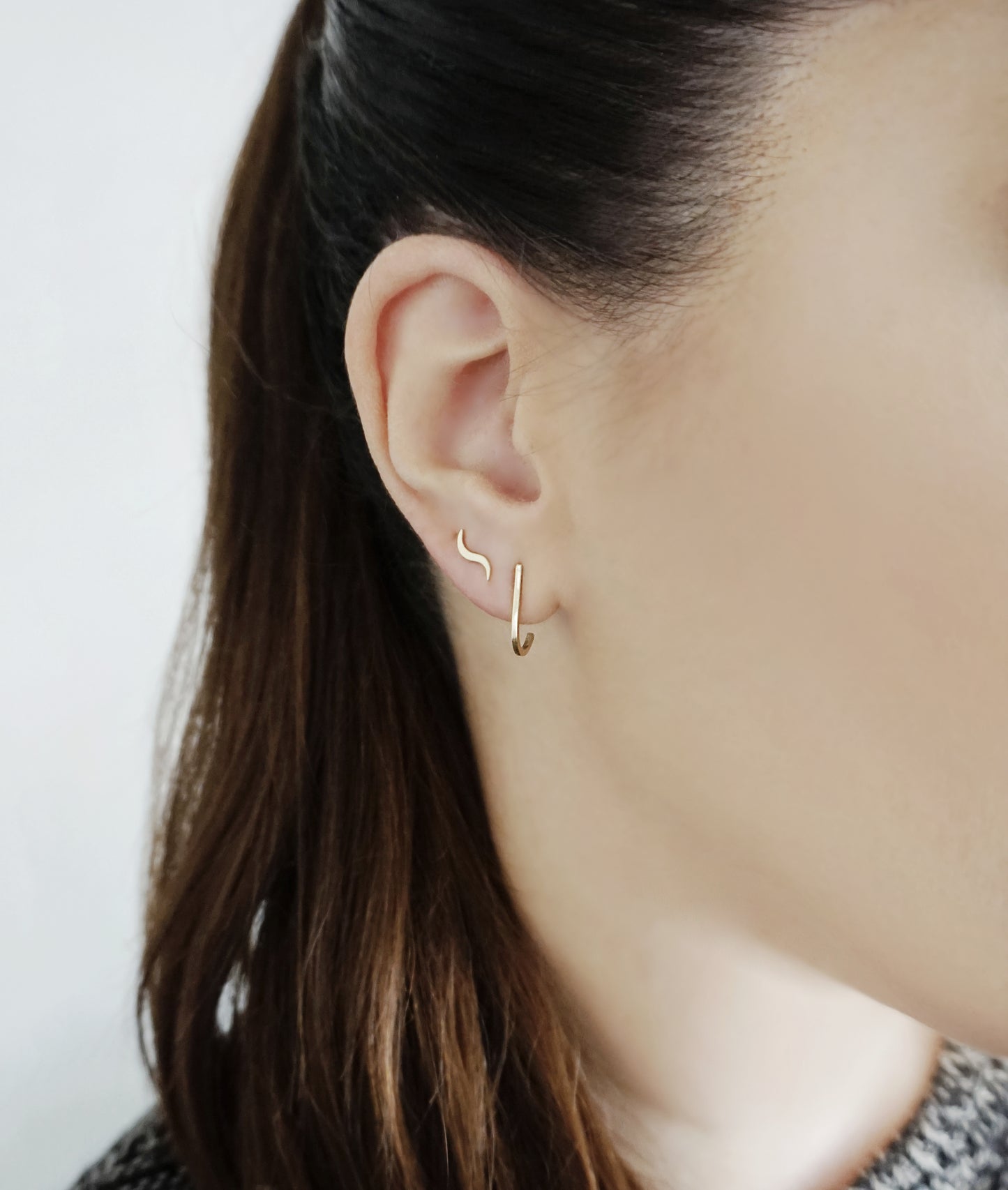 female wearing a solid yellow gold inverted suspender hook cuff earring and curved line stud