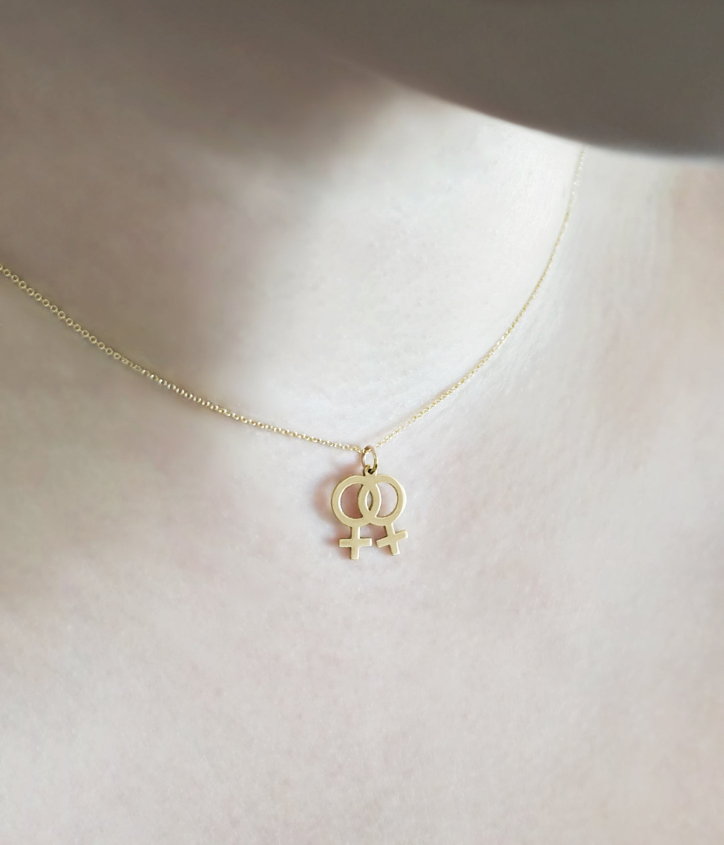 female wearing gold necklace with a small double female/venus lesbian symbol pendant
