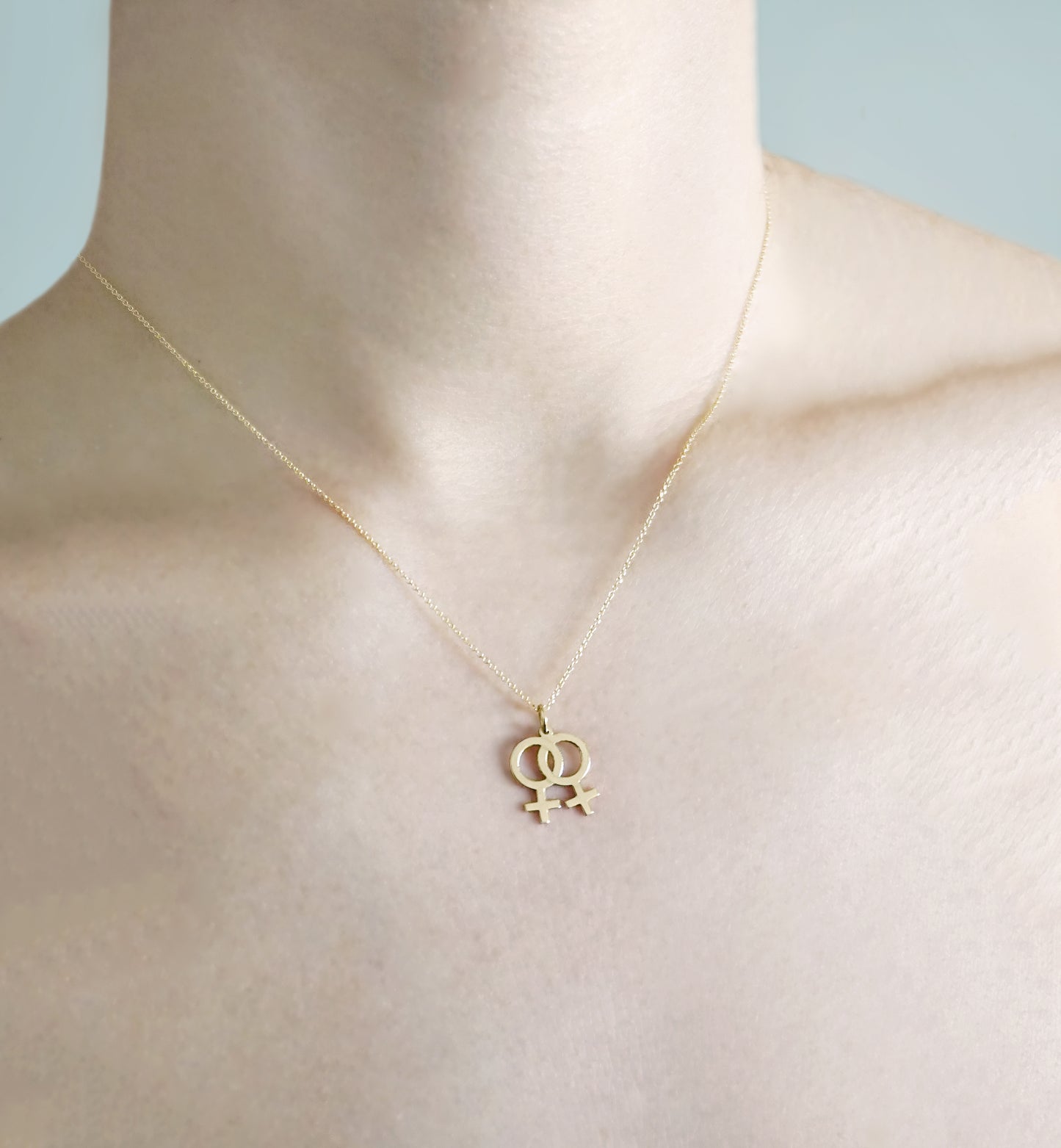 woman wearing a gold necklace with a small double female/venus lesbian symbol pendant
