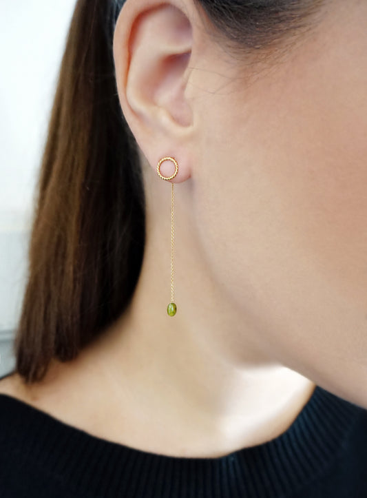female wearing yellow gold jacket earrings with a small twisted circle stud on the front of the earlobe and a long chain with a peridot bead at the end dangling on the back of the earlobe