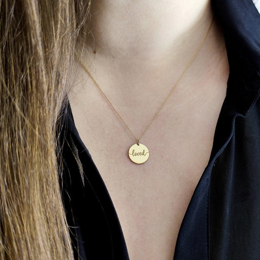 Gold necklace with a 'loved' pendant on a person wearing a black top.