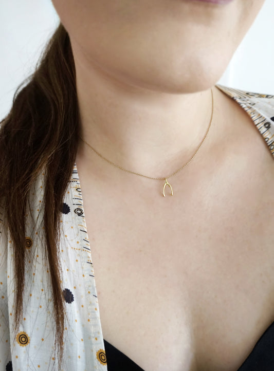 close up of a woman's neck wearing a dainty solid gold necklace with a tiny wishbone charm