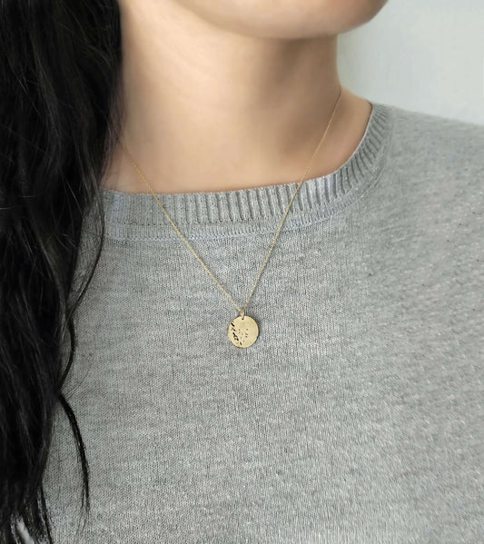 Gold necklace with a round hammered pendant worn by a female in a gray sweater.