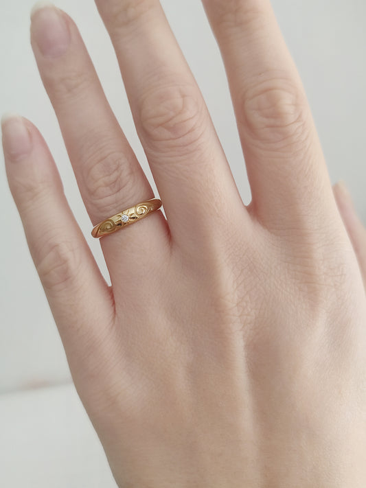 female hand wearing yellow gold dome band ring with floral designs and set with a white diamond with a star polaris setting