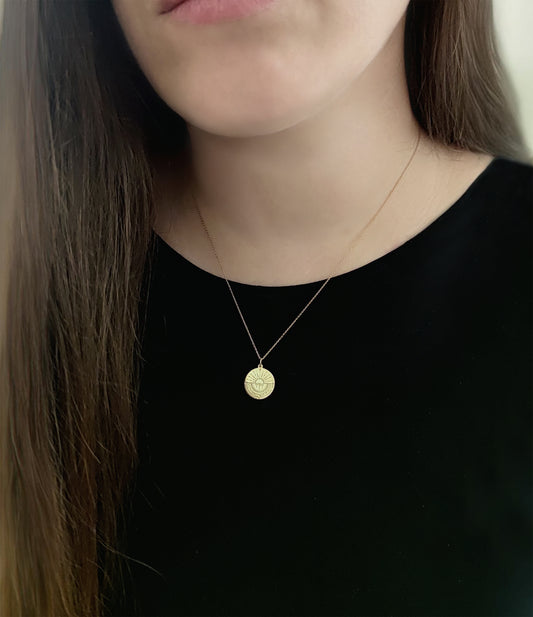 female wearing gold disc pendant necklace engraved with a compass and personalized coordinates