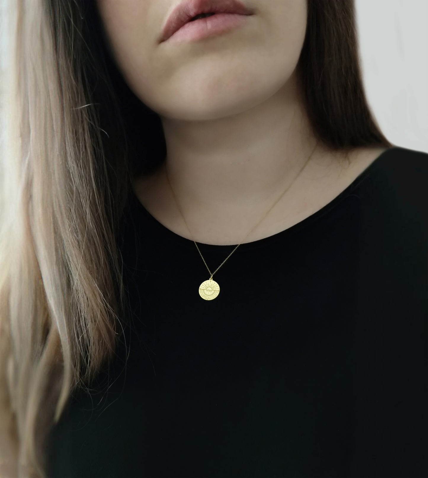 woman wearing gold disc pendant necklace engraved with a compass and personalized coordinates