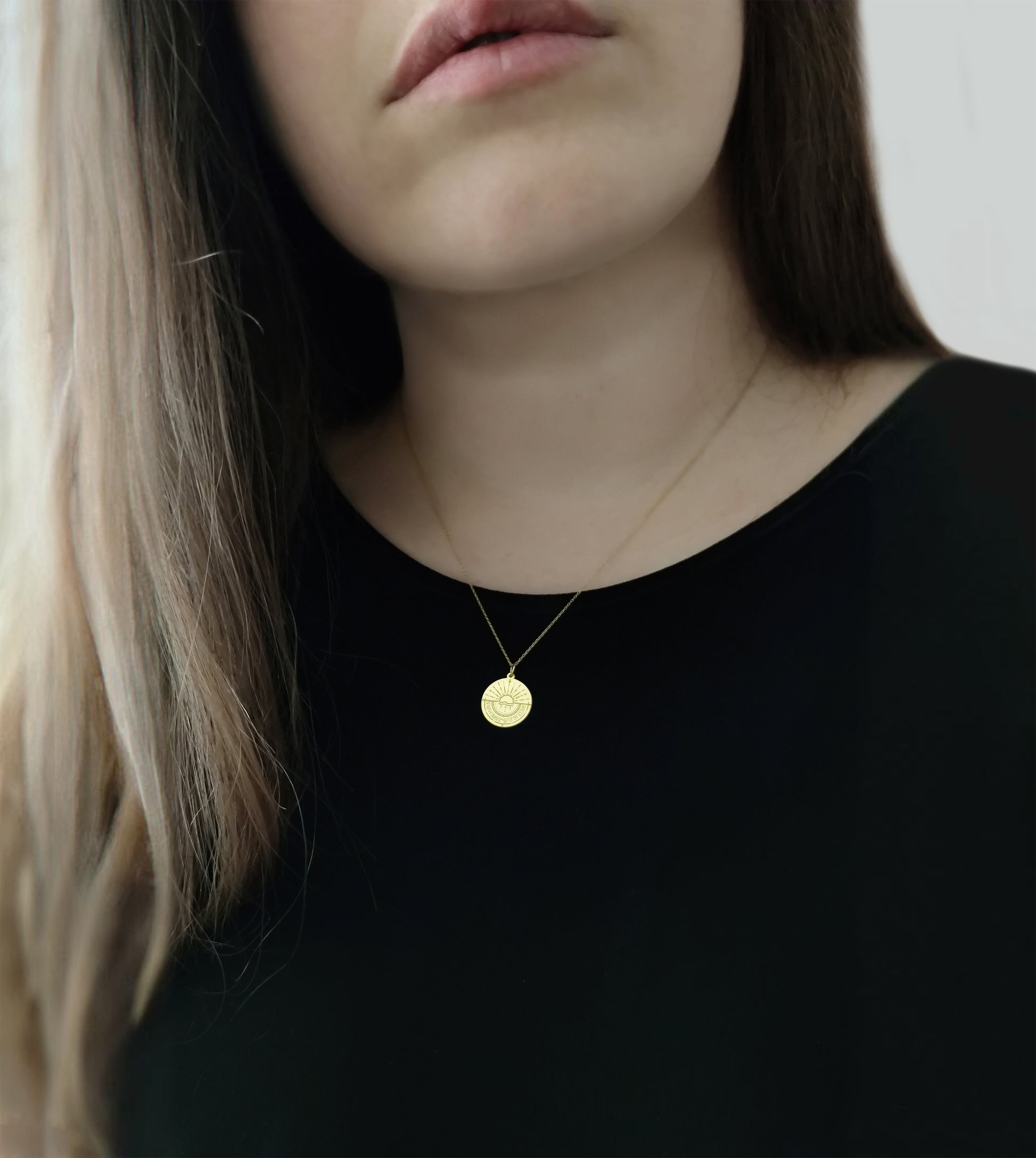 woman wearing gold disc pendant necklace engraved with a compass and personalized coordinates