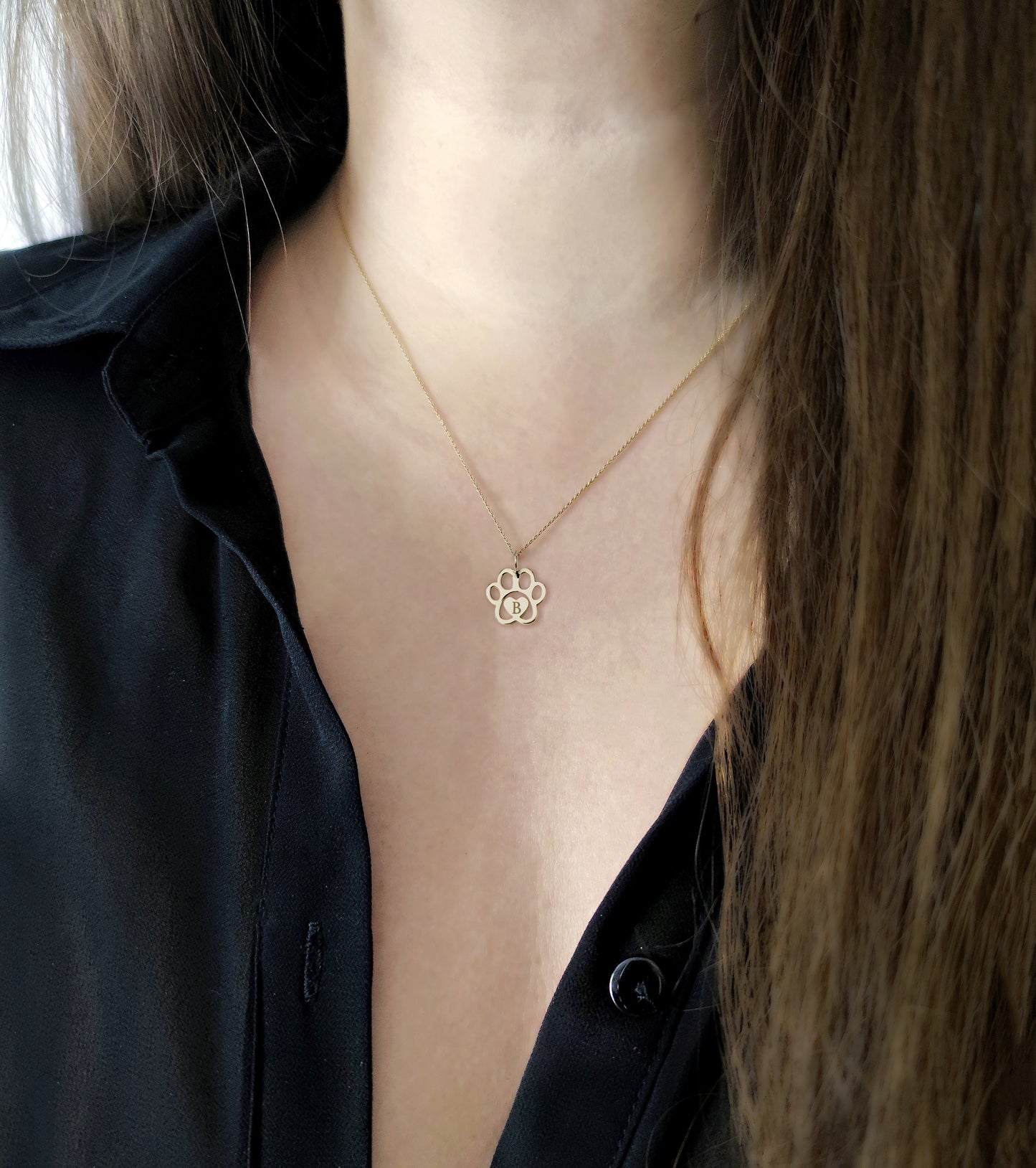 female wearing gold necklace with a dog paw print pendant engraved with a monogram