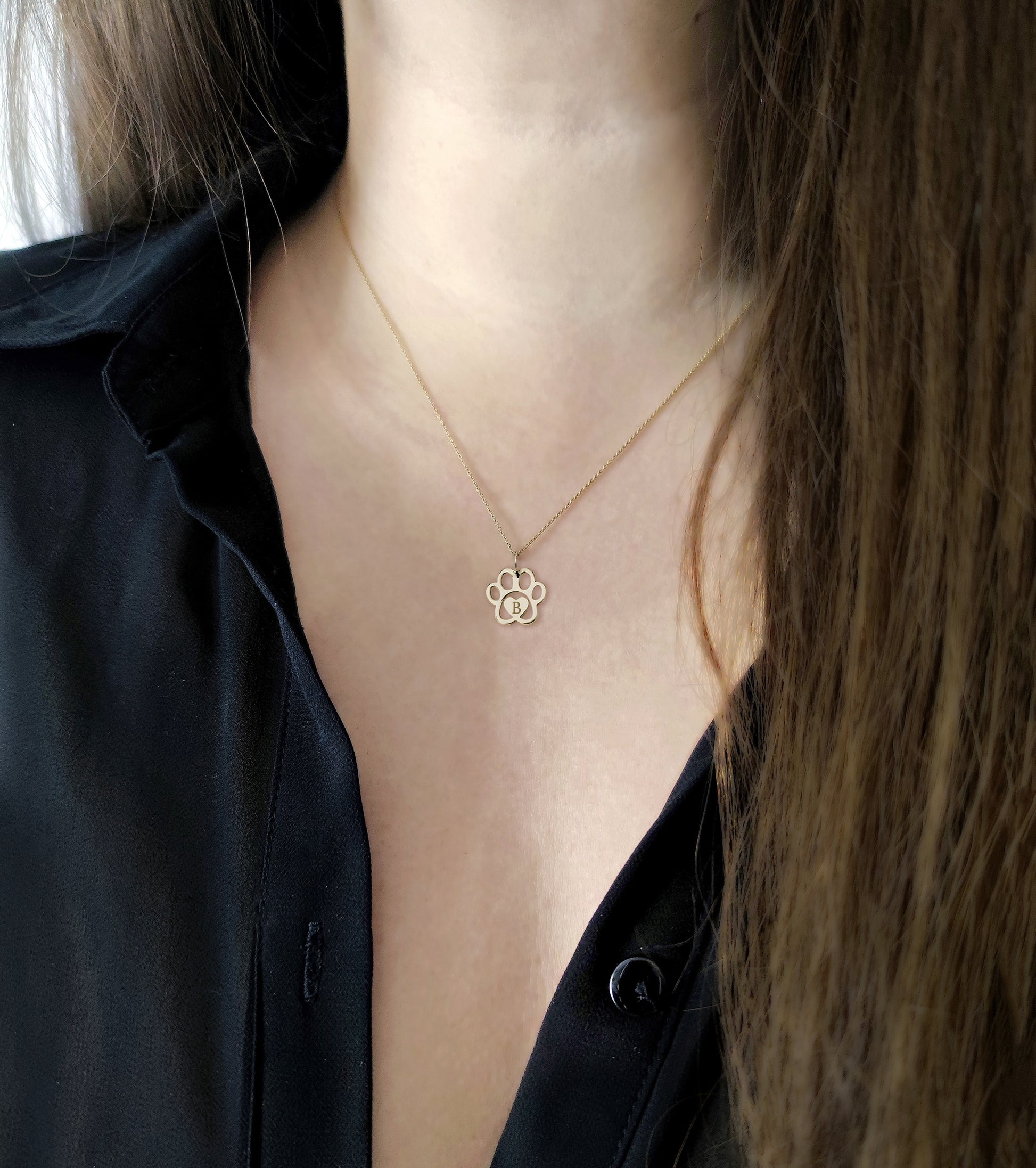 female wearing gold necklace with a dog paw print pendant engraved with a monogram