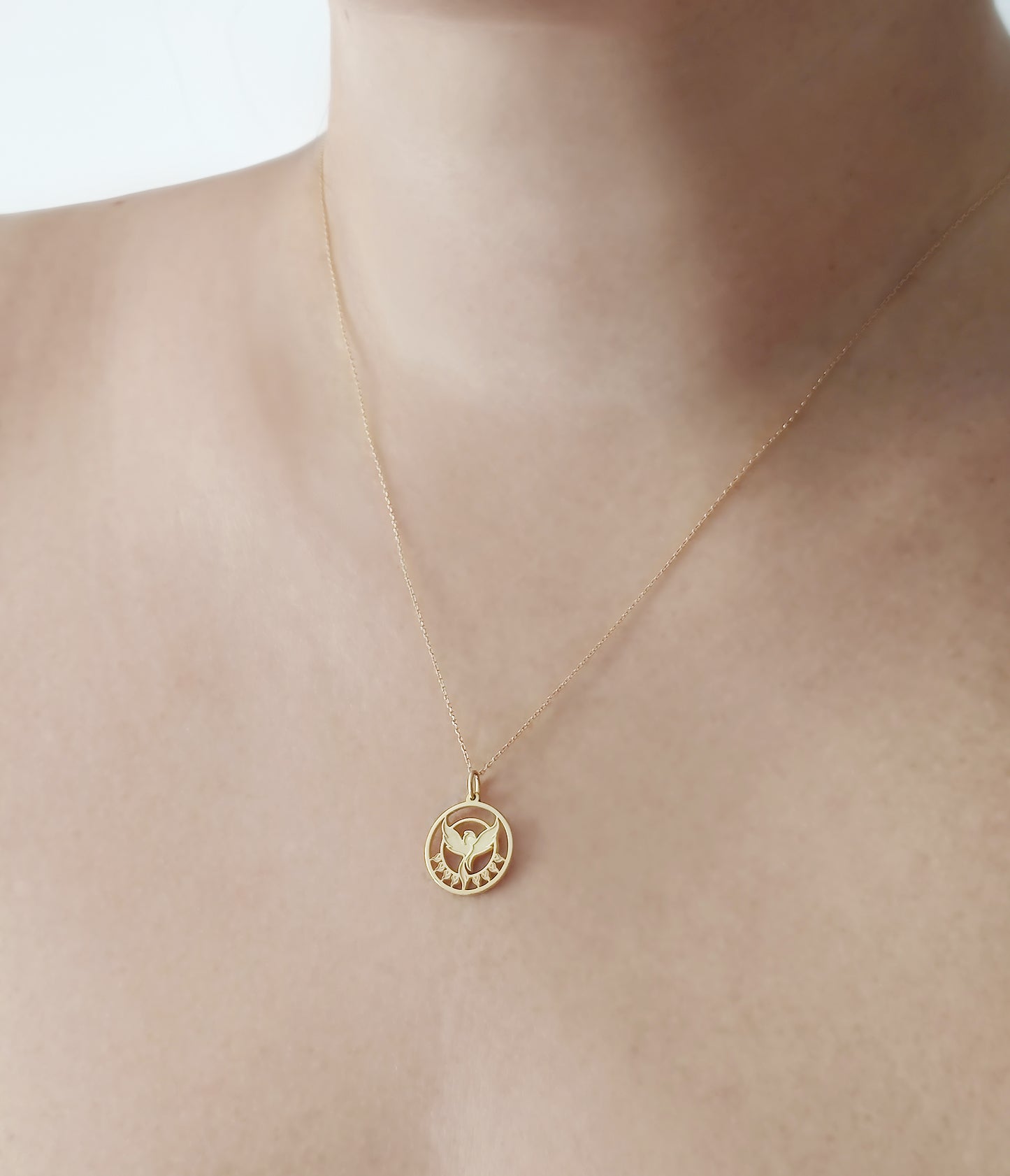 woman wearing a yellow gold necklace with a cutout phoenix firebird pendant rising from flames