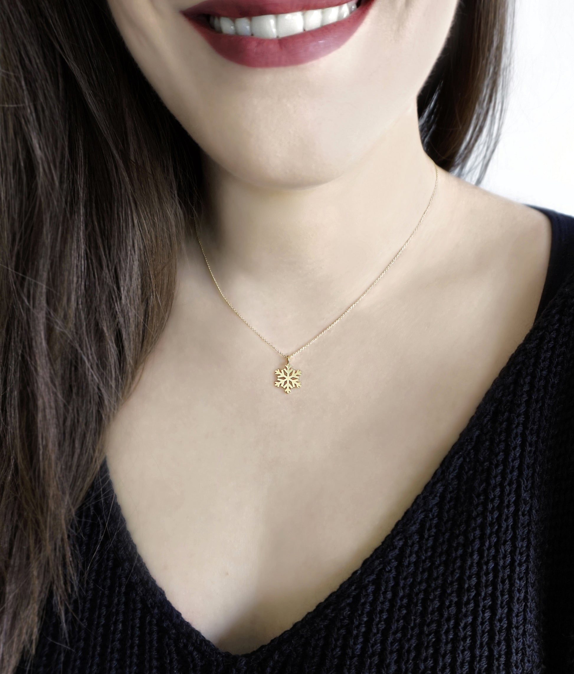 woman wearing gold necklace with a small pendant in the shape of a snowflake