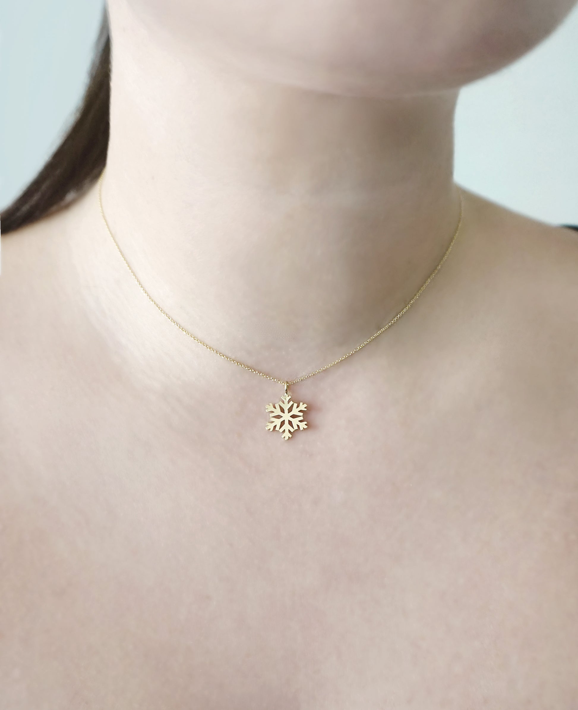 woman's neck wearing a gold necklace with a small pendant in the shape of a snowflake