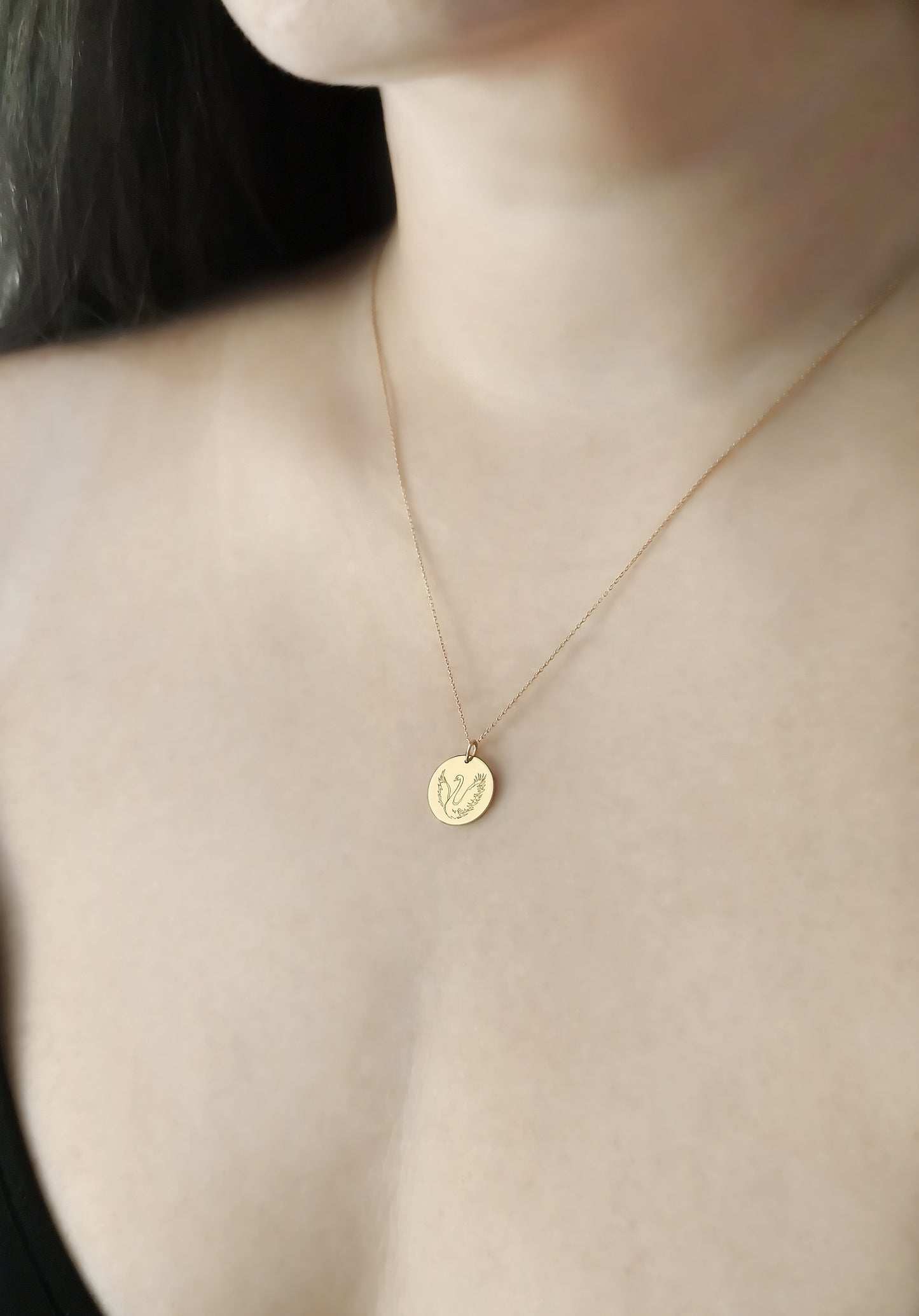 close up of a woman's neck wearing a yellow gold necklace with a 14mm disc pendant engraved with a swan