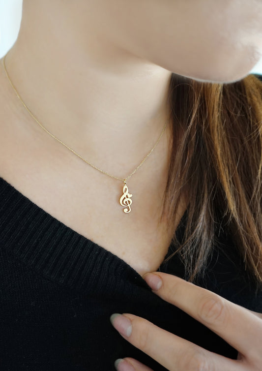 female wearing a gold necklace with a treble clef pendant adorned with a tiny heart