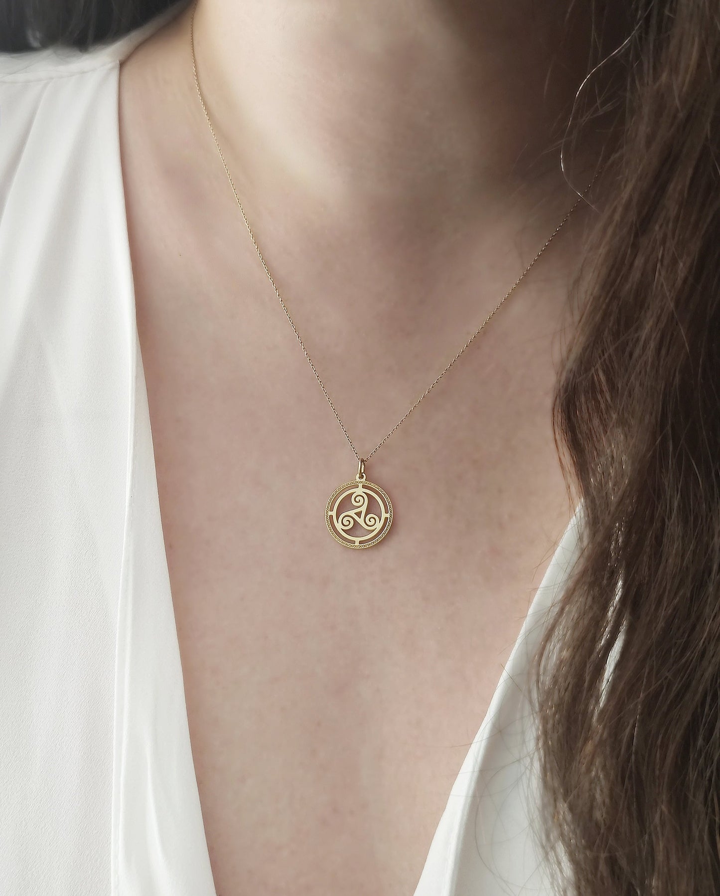 close up of a woman's neck wearing a gold necklace with a circular triskelion celtic knot pendant with cutouts