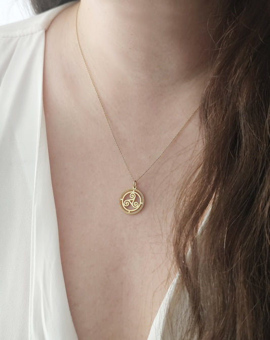 close up of a woman's neck wearing a yellow gold necklace with a cutout triskelion celtic knot pendant