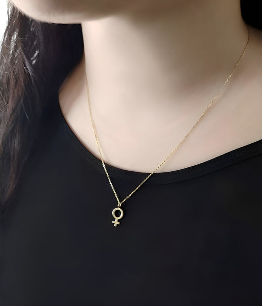 close up of a woman's neck wearing a yellow gold necklace with a small female venus symbol pendant