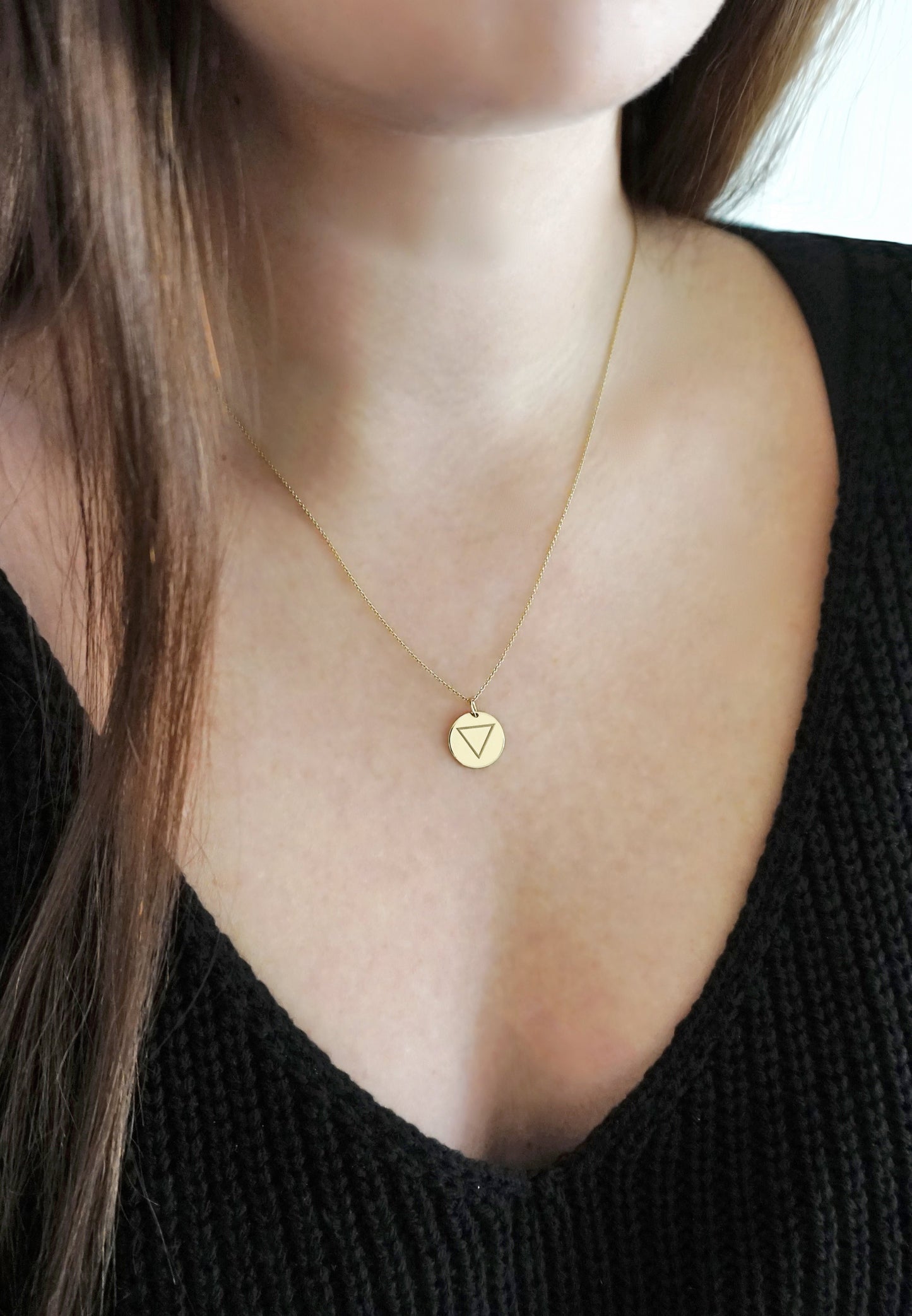 female wearing a yellow gold necklace with a 14mm disc pendant engraved with the water element symbol