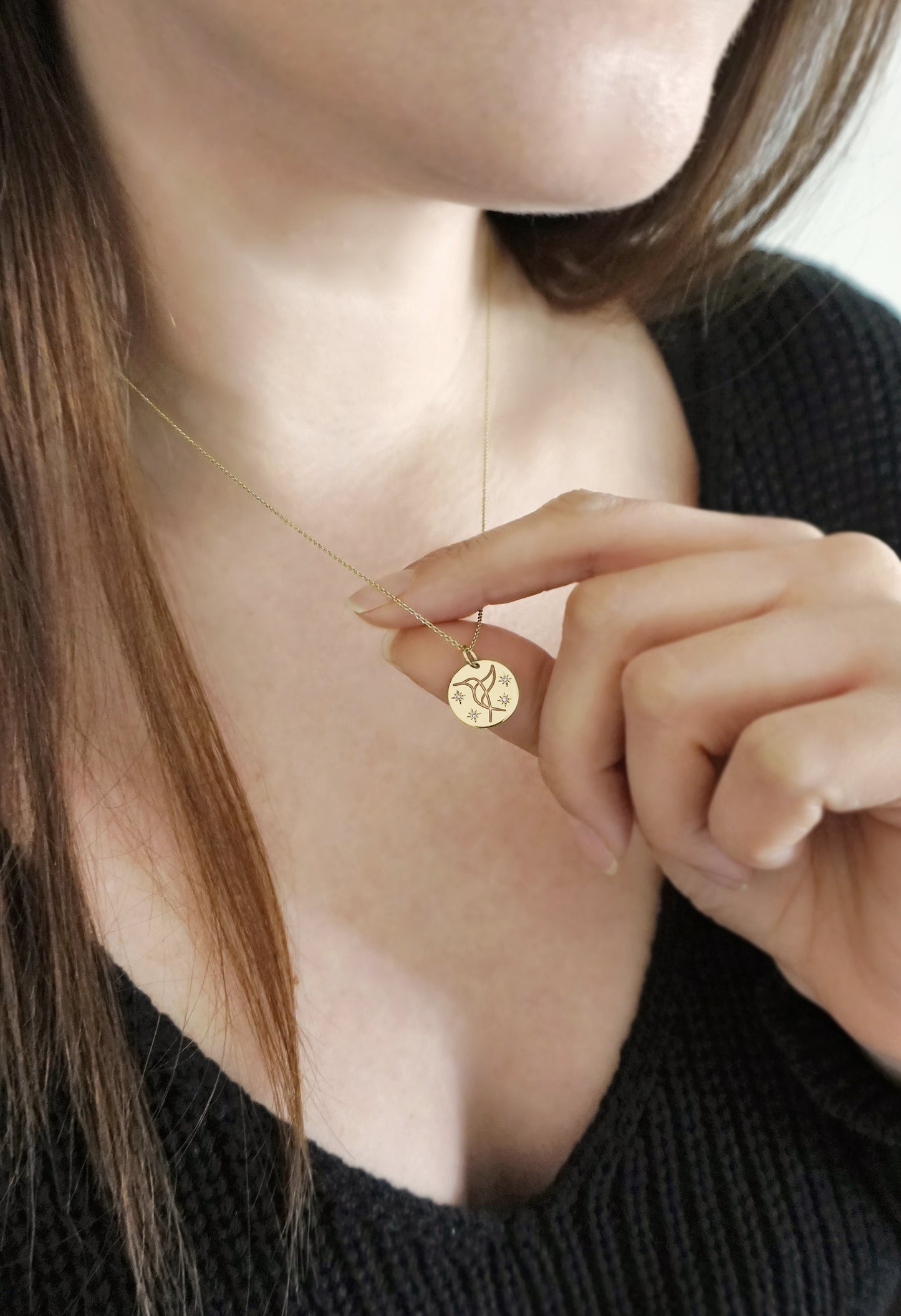 woman wearing and holding solid gold necklace with 14mm disc pendant engraved with a hummingbird and set with four white diamonds with a star setting