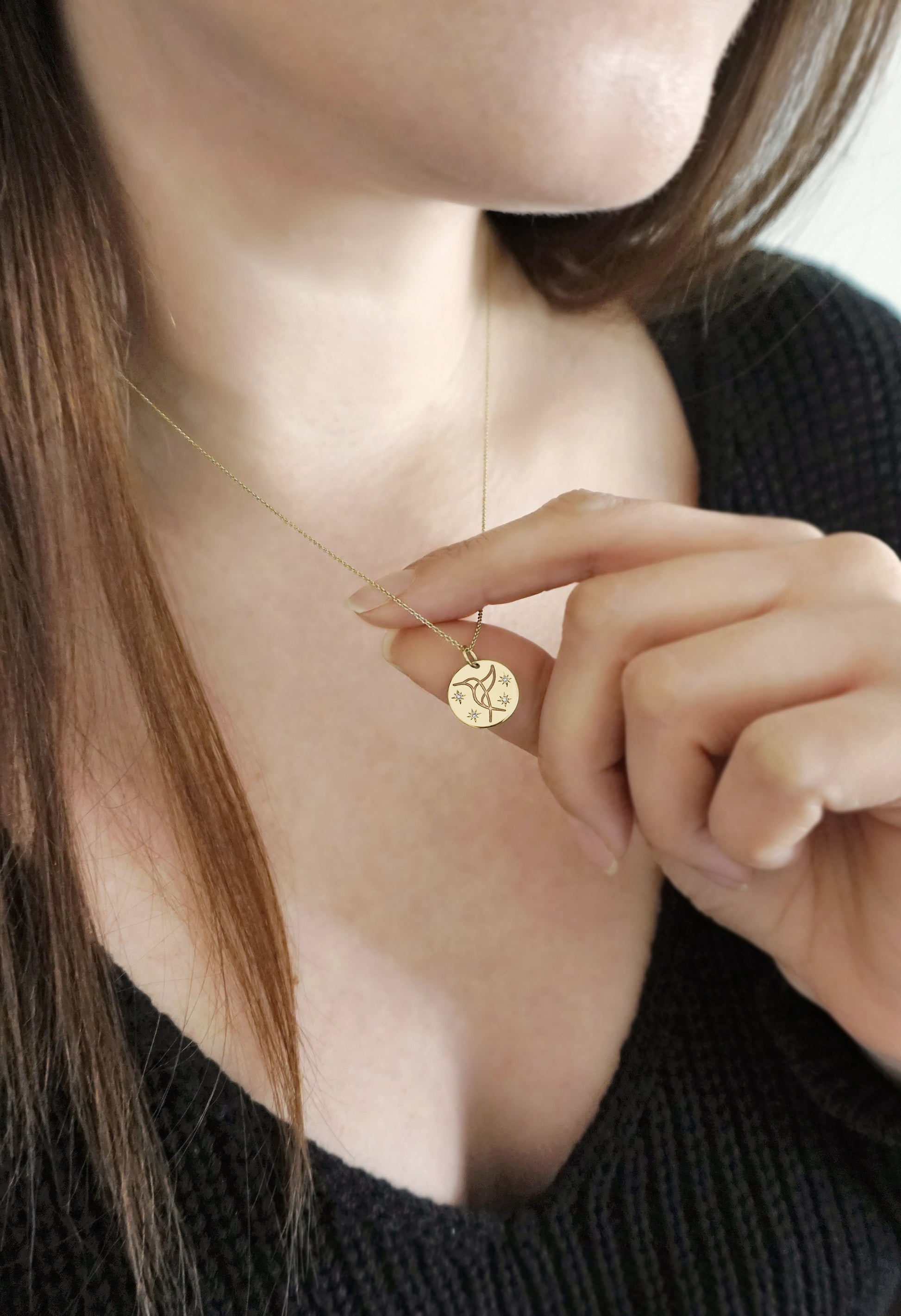 woman wearing and holding solid gold necklace with 14mm disc pendant engraved with a hummingbird and set with four white diamonds with a star setting
